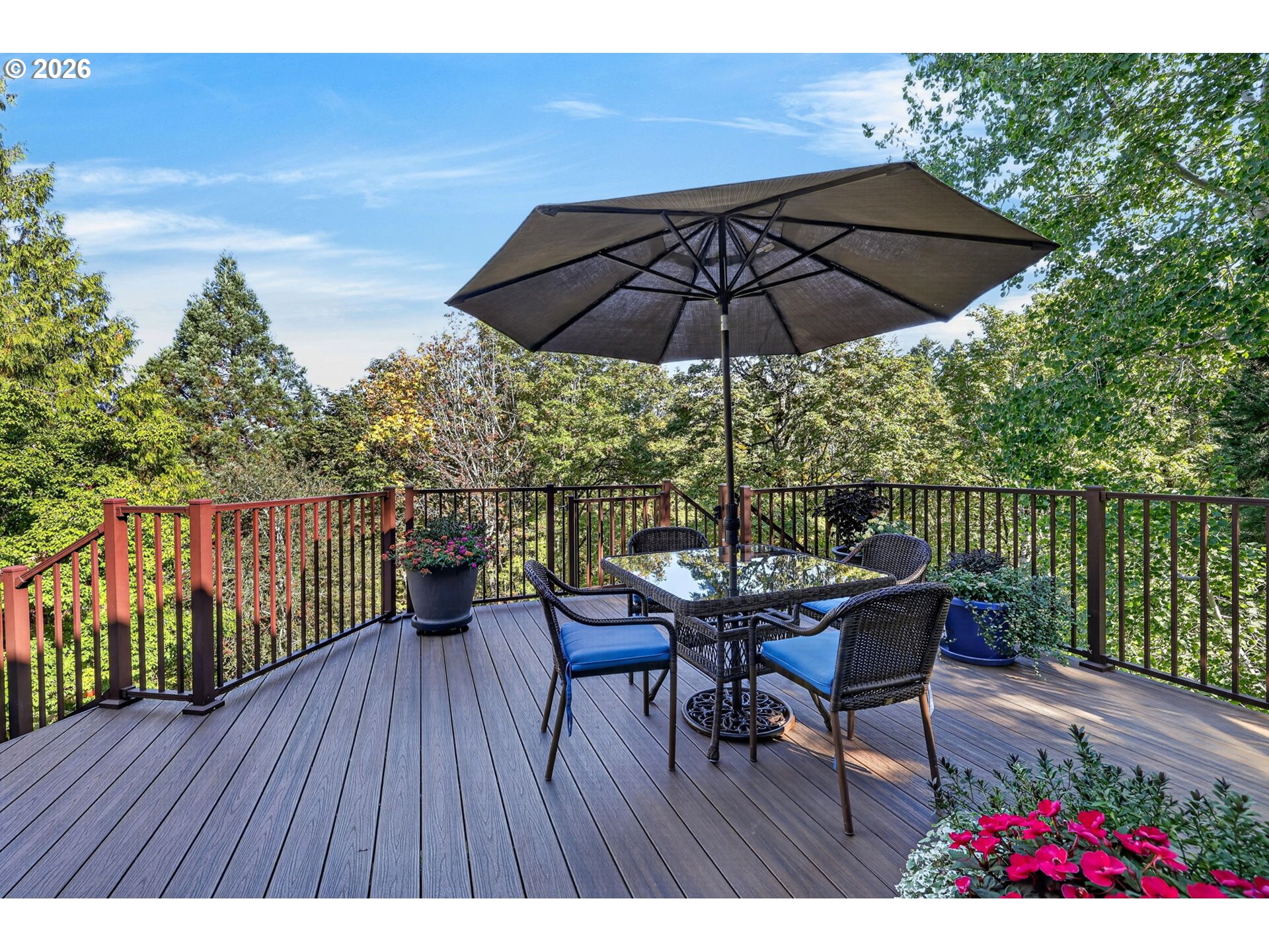 Furnished deck with a large umbrella and dining set overlooking leafy trees.