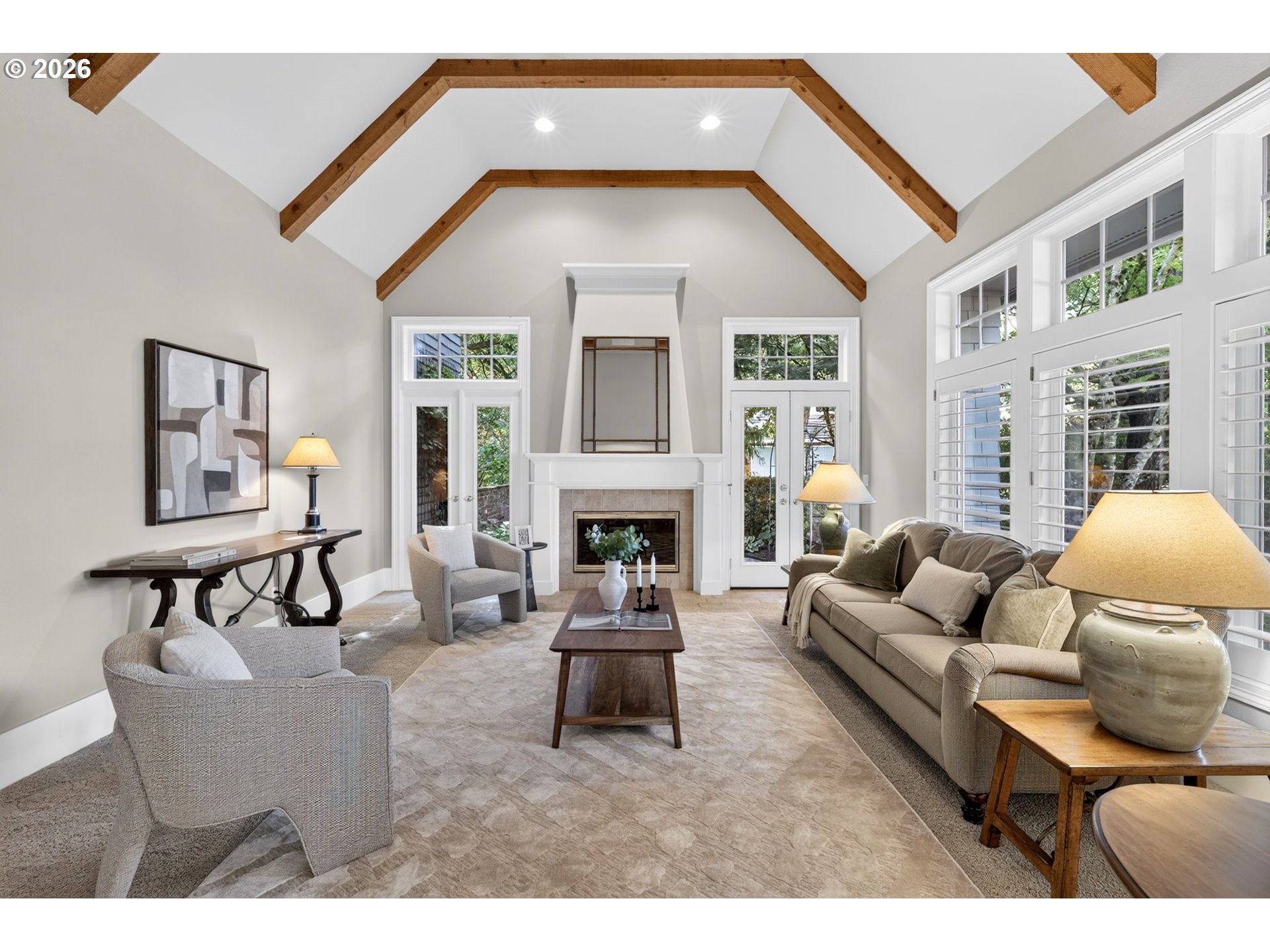Living room with vaulted wood-beamed ceiling, fireplace, and large shuttered windows.