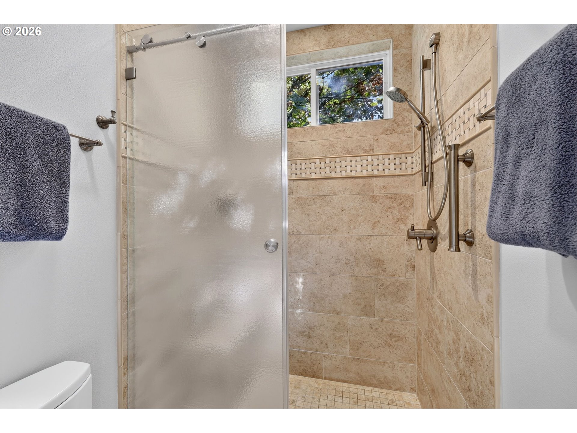Tan tiled walk-in shower with frosted glass door, handheld showerhead, and window.