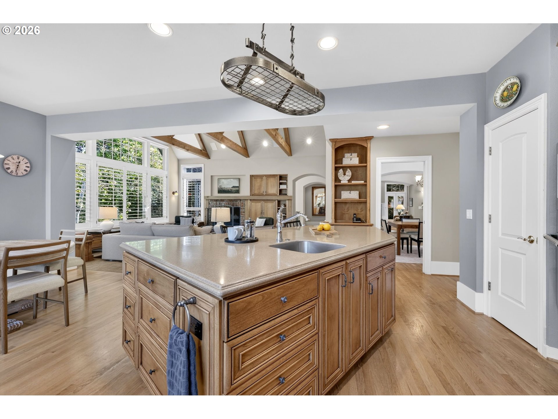 Kitchen with a large wood island, exposed ceiling beams, and tall shuttered windows overlooking the living area.