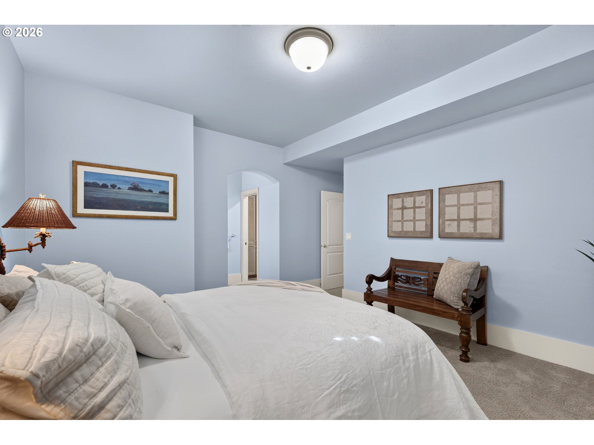Bedroom with a large white bed, pale blue walls, and a dark wooden bench.