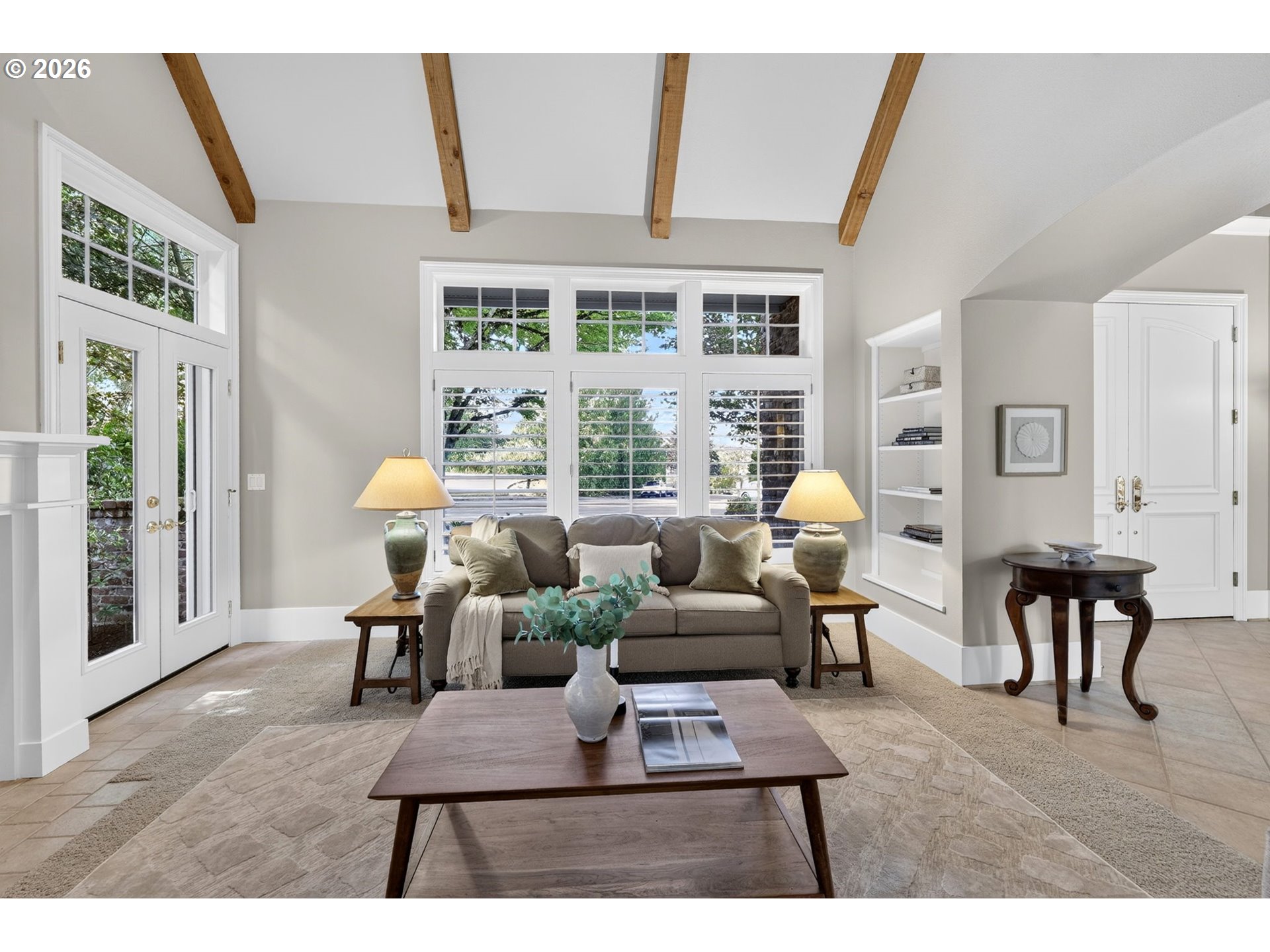 Living room with exposed ceiling beams, tall shuttered windows, and a neutral sofa.