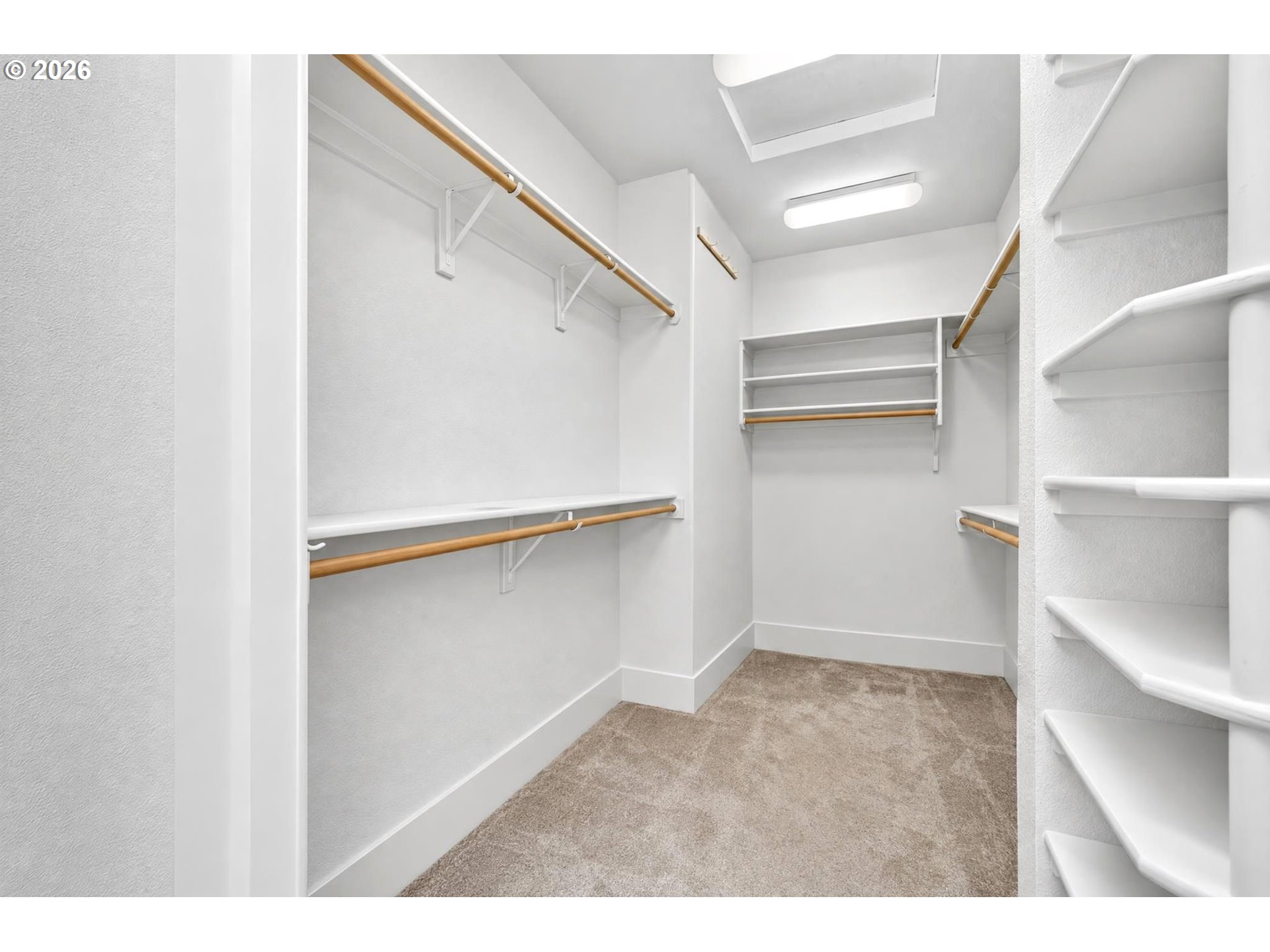 Walk-in closet with built-in shelves, wooden hanging rods, and beige carpet.