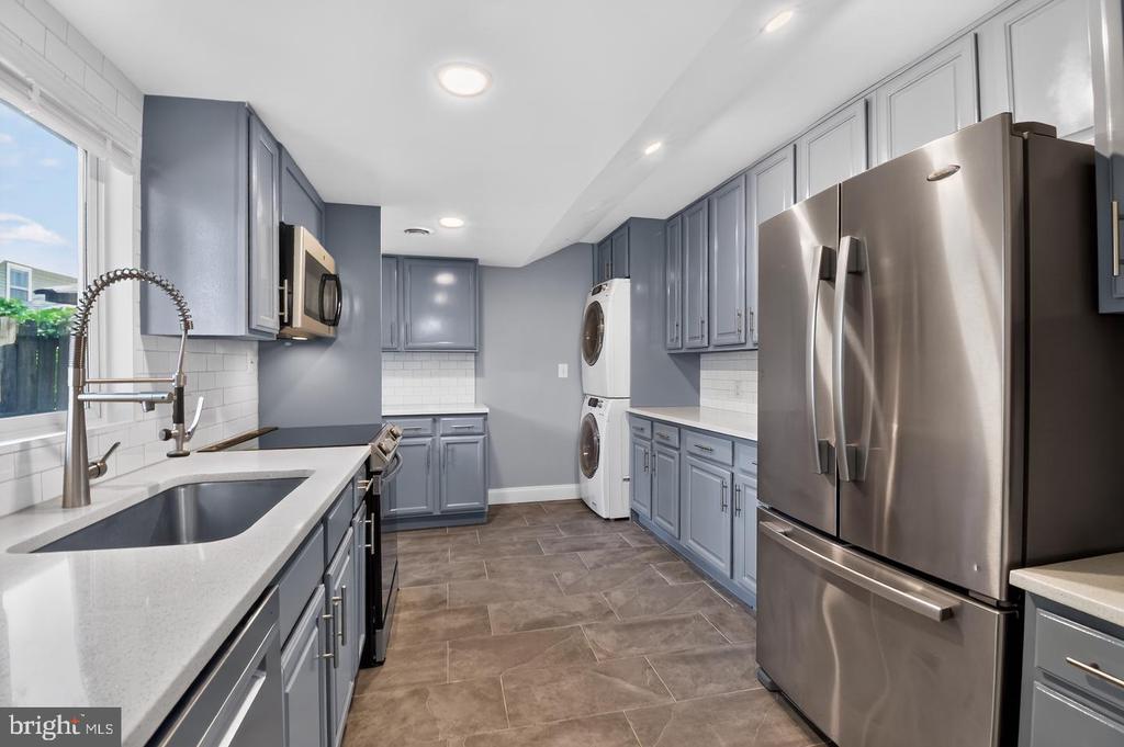 Kitchen with blue-gray cabinets, a large window, stainless steel refrigerator, and stacked washer and dryer.