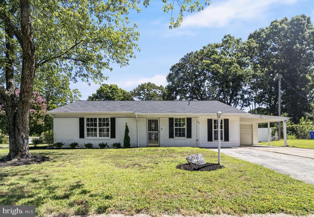 Single-story white brick house with dark shutters, a front lawn, and a driveway beside a carport.