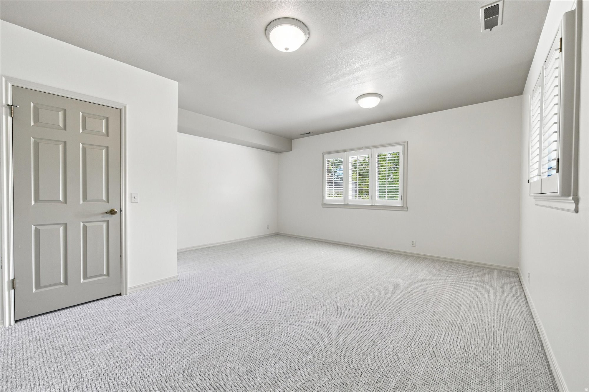 Empty bedroom with light gray carpet and plantation-shuttered windows.