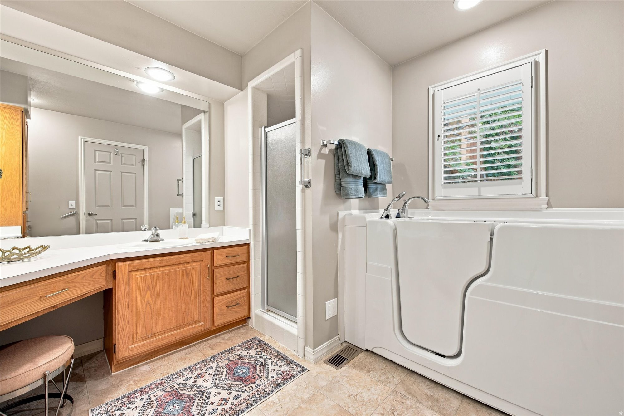 Bathroom with a walk-in tub, glass shower, and warm wood vanity.