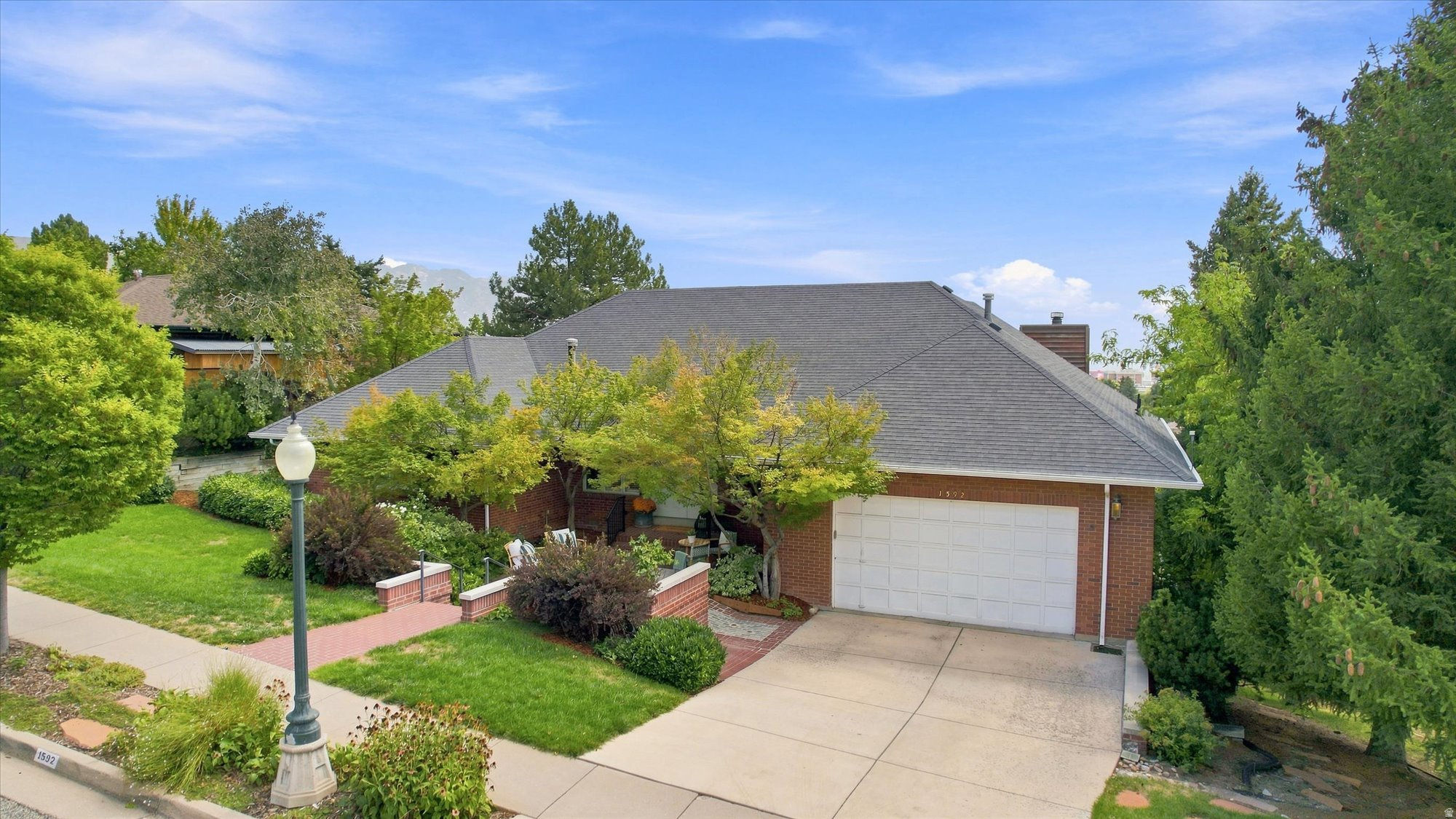 Brick house with a gray roof, white double garage door, landscaped yard, and brick patio.
