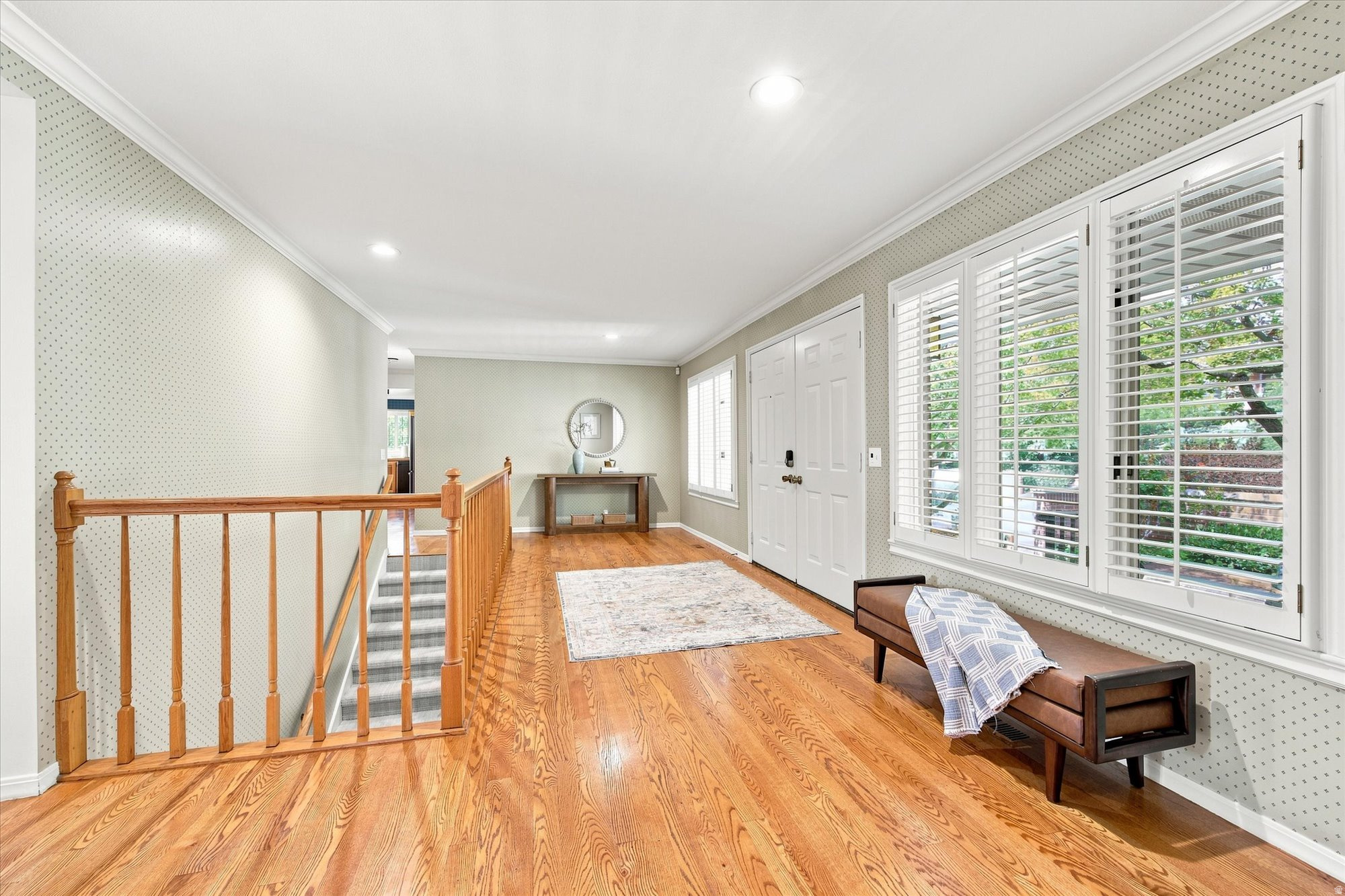 Foyer with hardwood floors, wooden stair railing, console table, and large shuttered windows.
