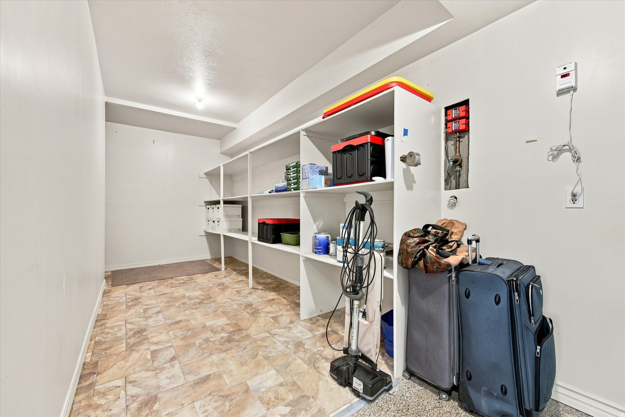 Storage room with built-in shelving, patterned tile floor, luggage, and a vacuum cleaner.