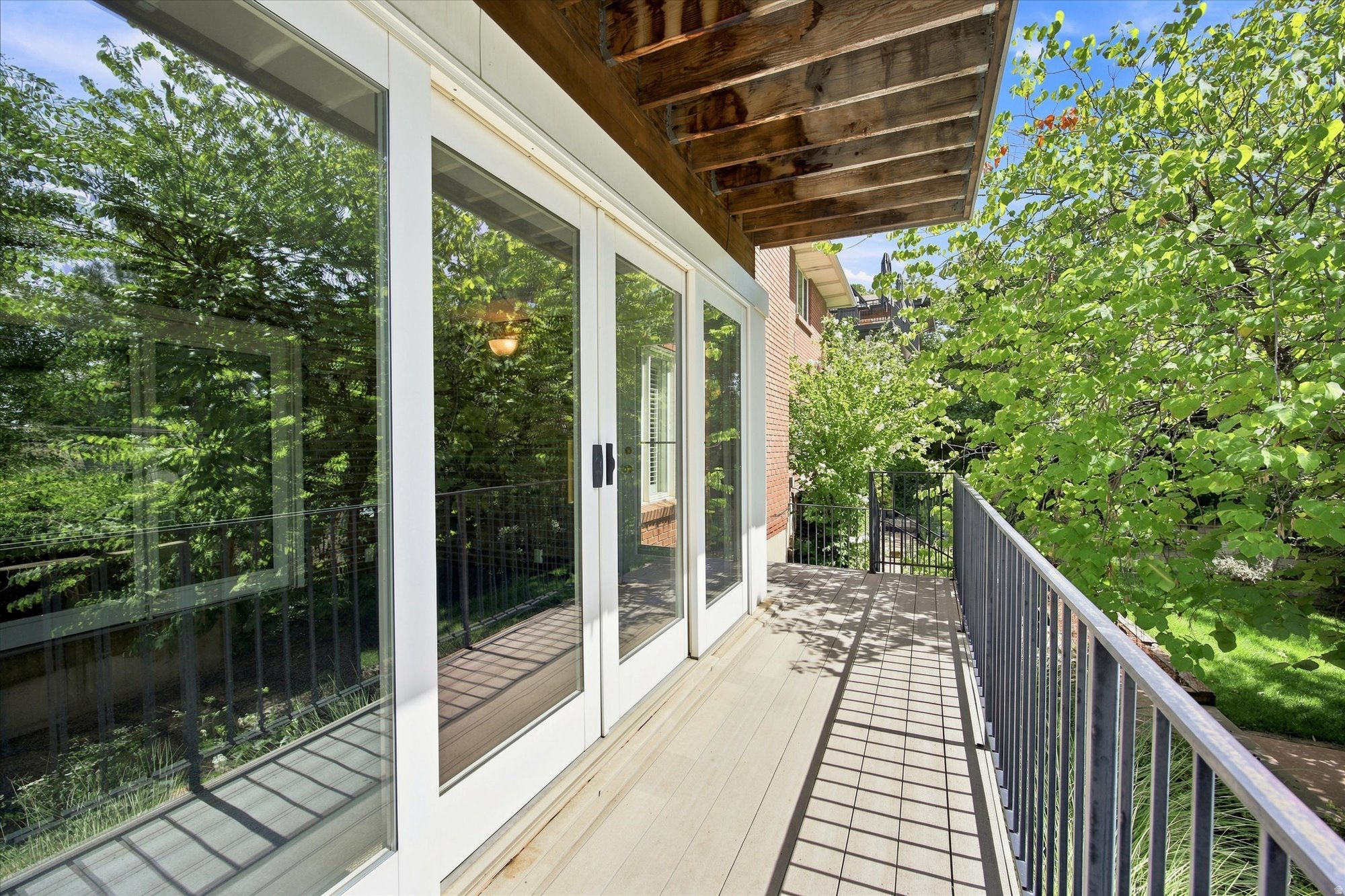 Side deck with sliding glass doors, a timber overhang, and leafy trees beyond the railing.