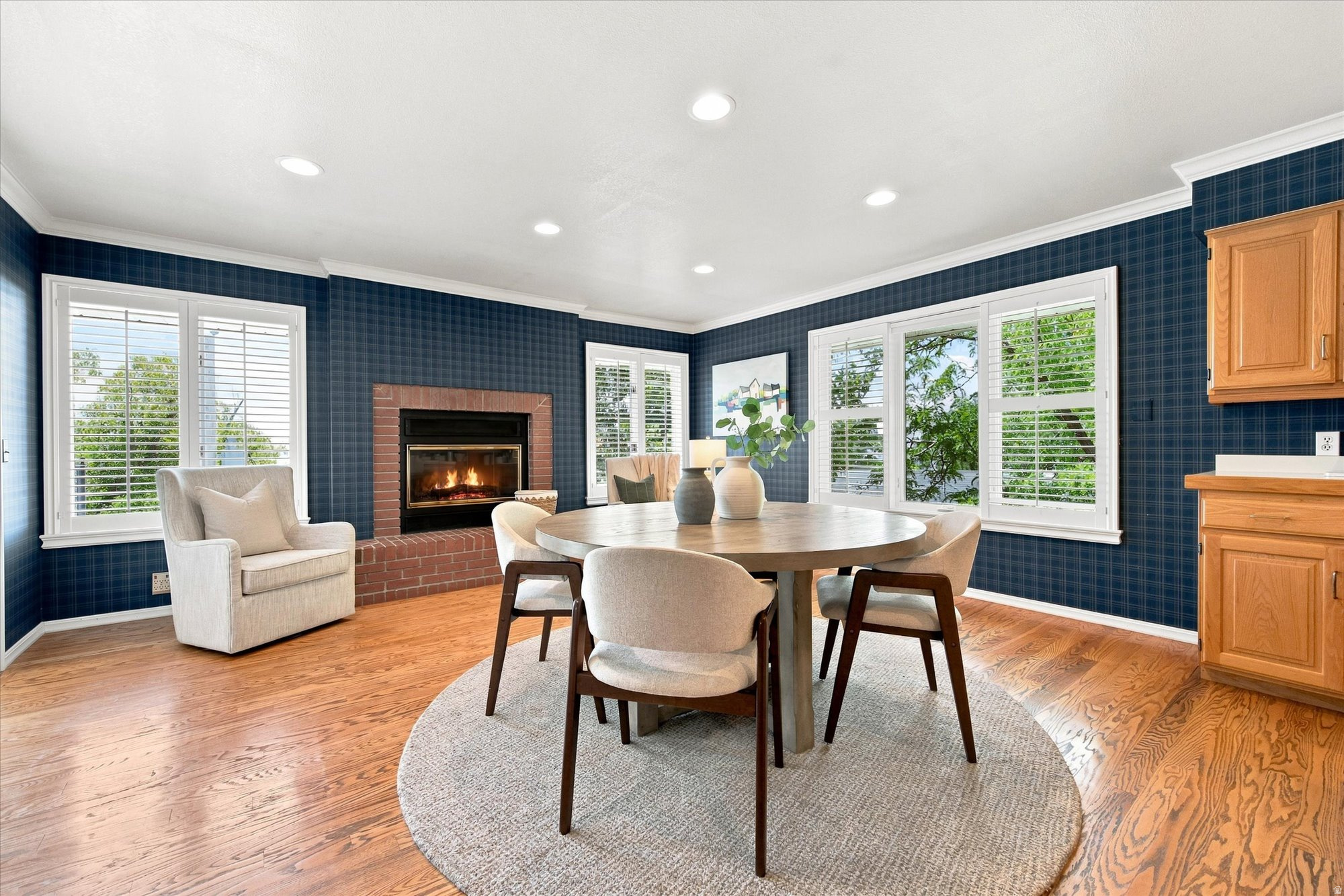 Dining room with a round table, brick fireplace, navy plaid walls, and shuttered windows.