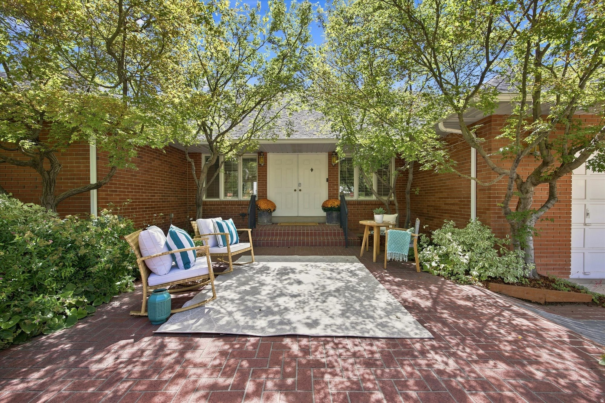 Red-brick home entrance beneath leafy trees, with a brick courtyard and staged outdoor seating.