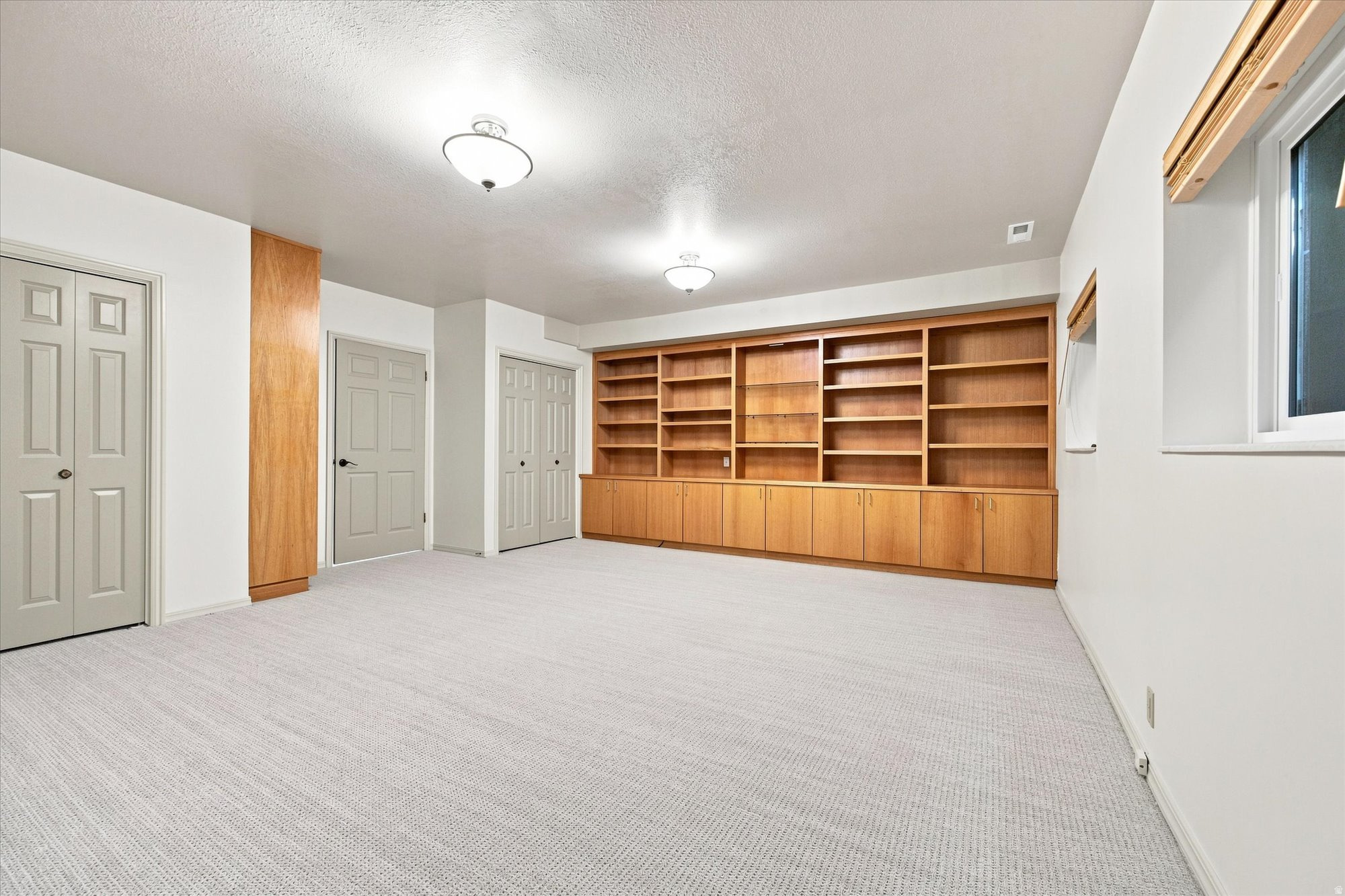 Empty carpeted room with built-in wooden bookshelves and cabinets.
