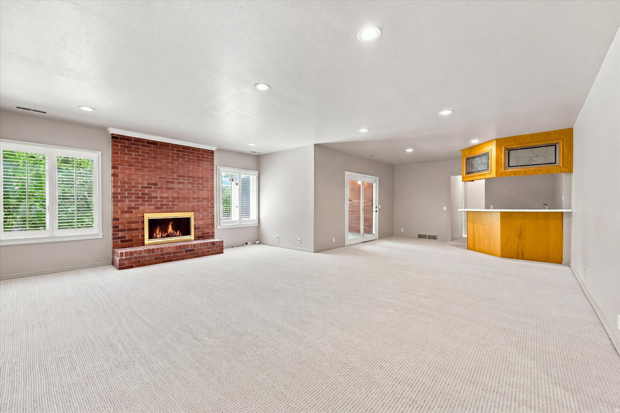 Vacant living room with a brick fireplace, shuttered windows, and a built-in wood bar.