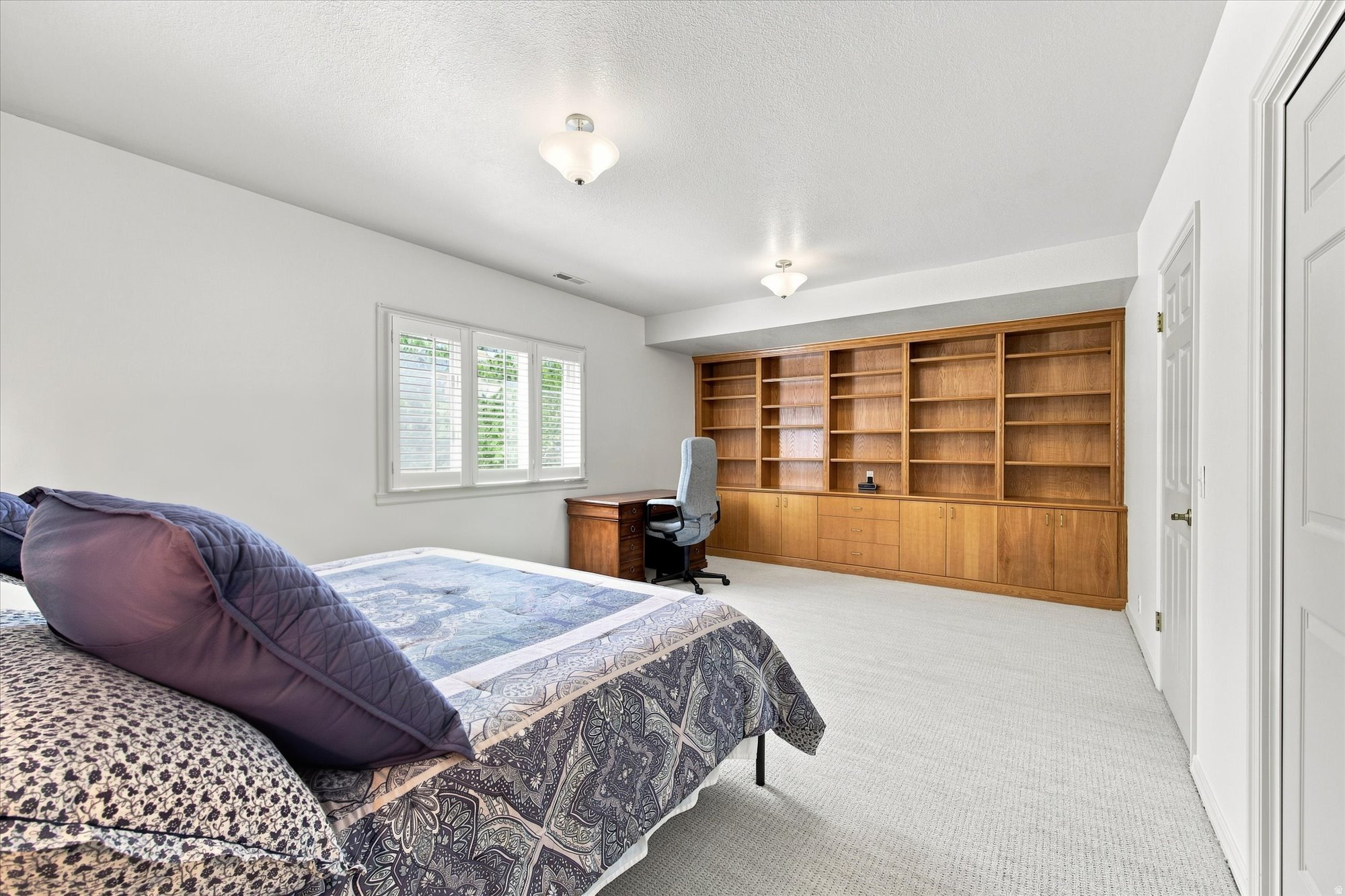 Bedroom with a patterned bed and built-in wooden bookshelves, cabinets, and desk.