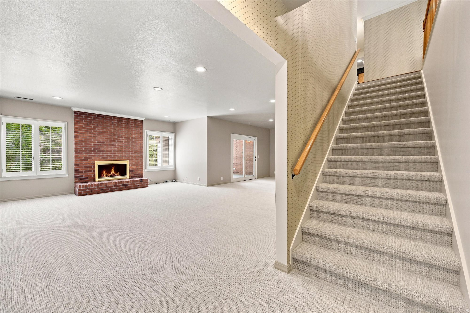Vacant living room with brick fireplace and carpeted staircase.