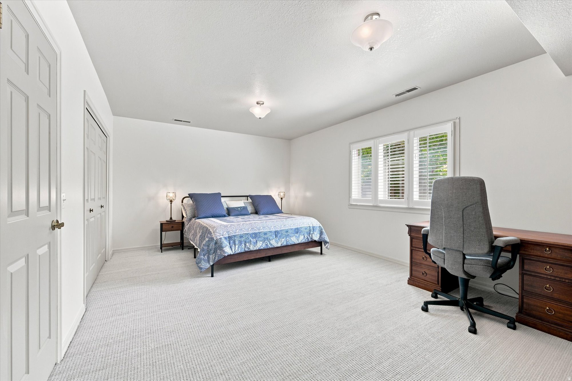 Furnished bedroom with a blue-patterned bed, shuttered windows, and a wooden desk.