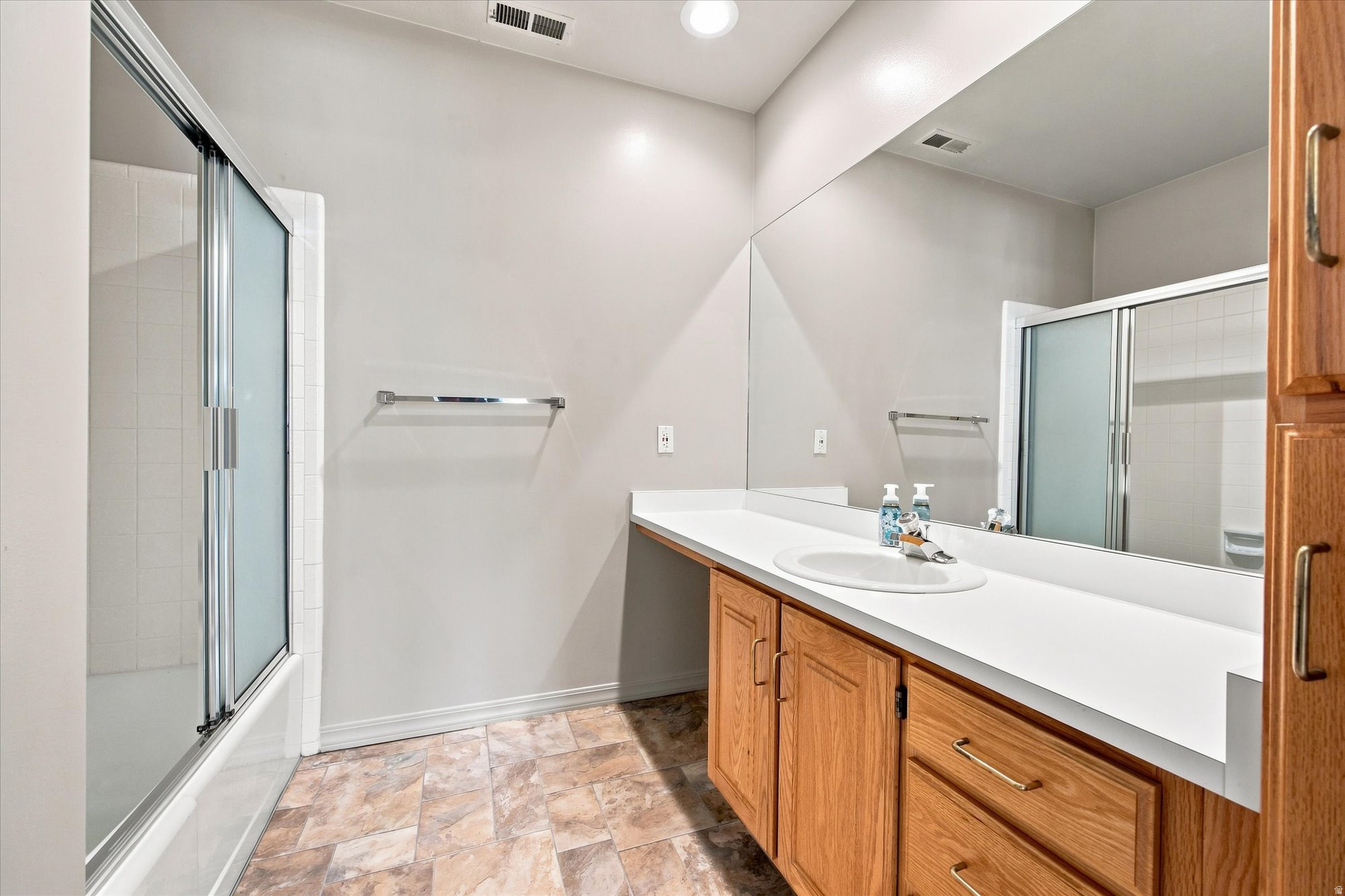 Bathroom with a long wood vanity, large mirror, and frosted-glass shower enclosure.