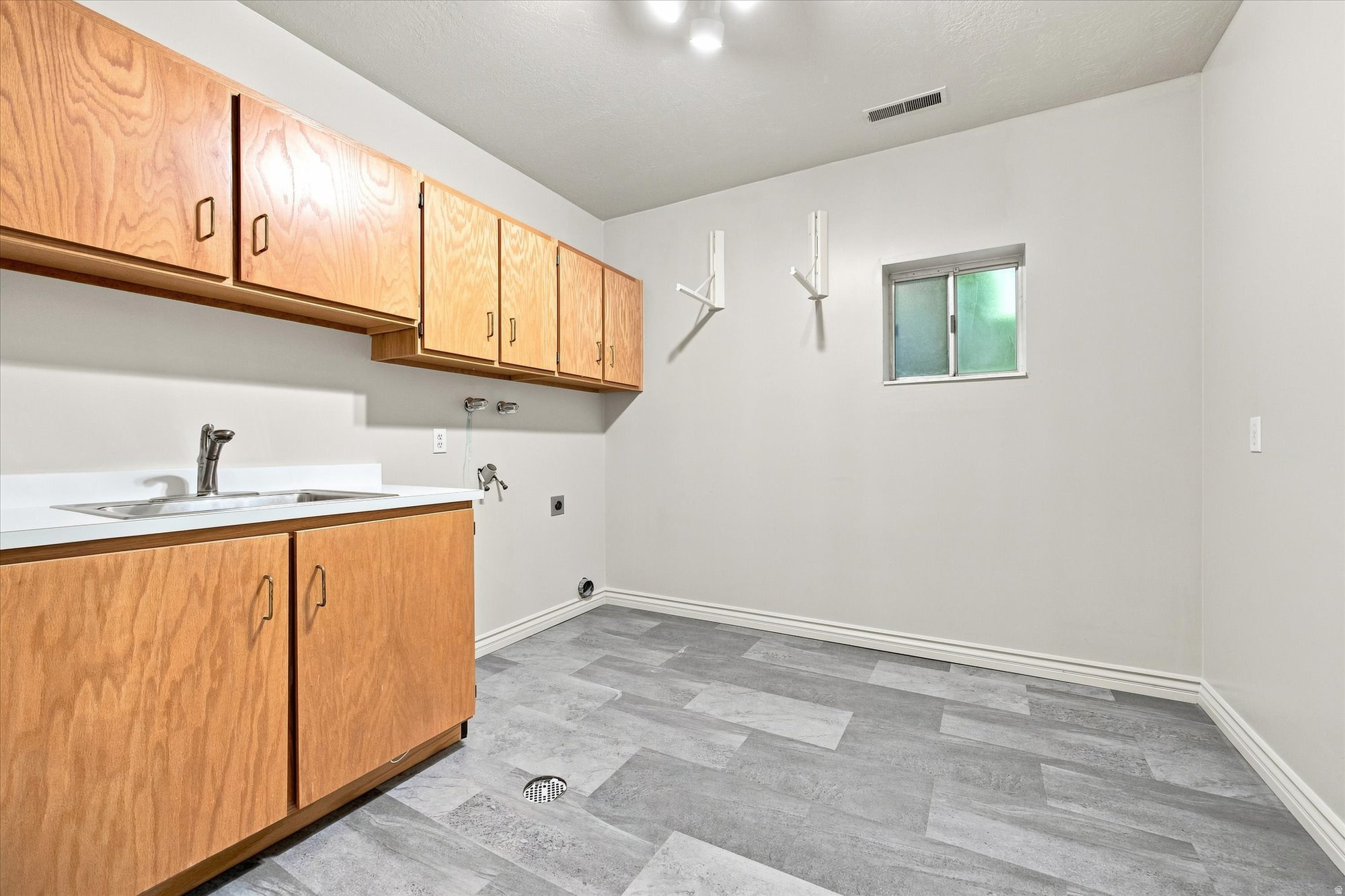 Laundry room with wood cabinets, utility sink, appliance hookups, and gray tile flooring.