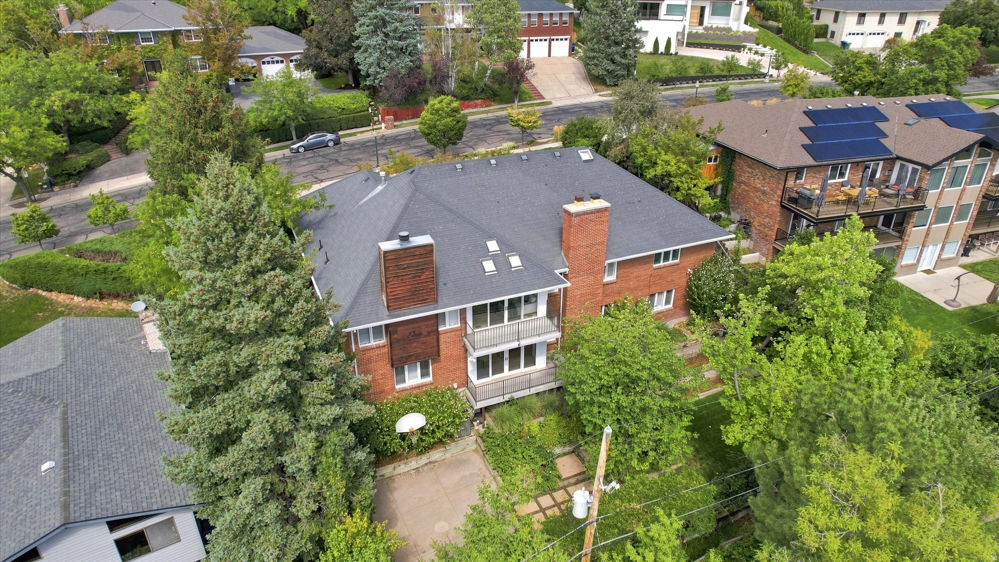 Aerial view of a red-brick home with two balconies and a tree-filled yard.