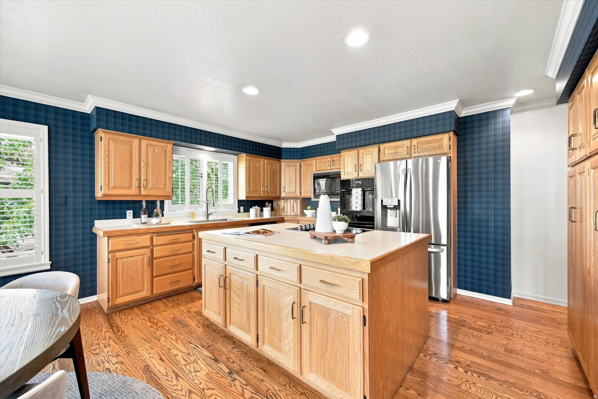 Kitchen with a large wood island, stainless steel appliances, hardwood floors, and dark blue plaid wallpaper.
