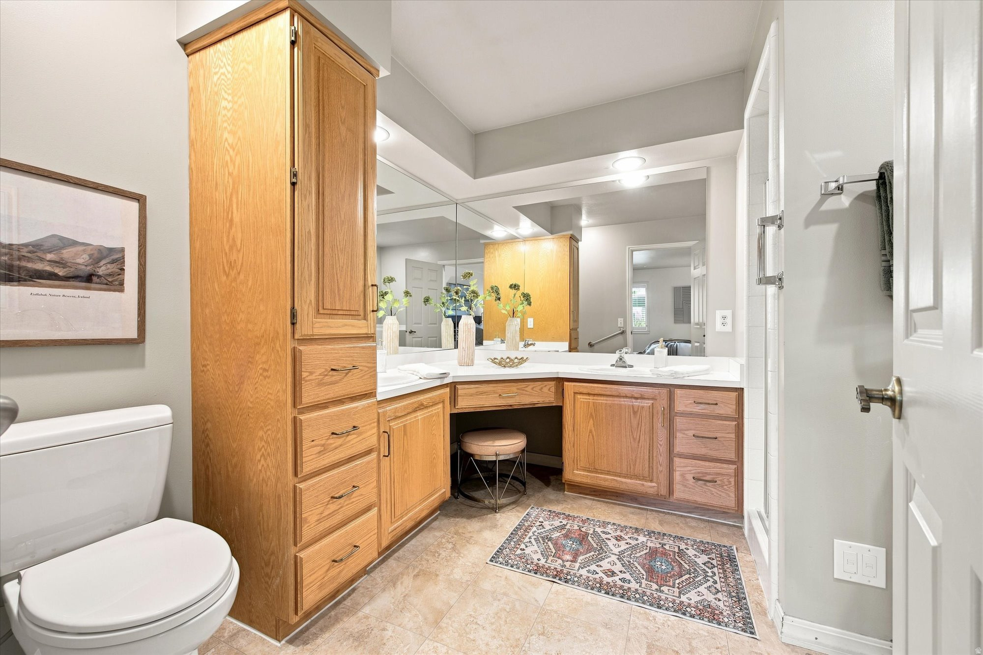 Bathroom with extensive wood cabinetry, mirrored vanity, glass shower enclosure, and patterned rug.