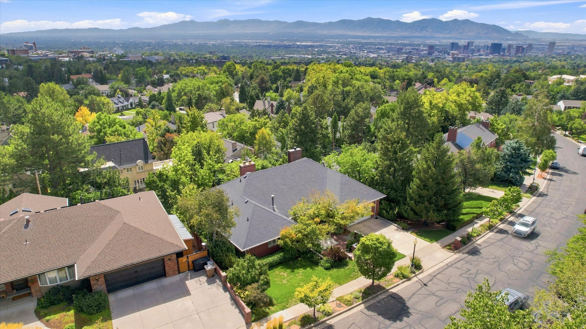 Aerial view of a leafy Salt Lake City neighborhood, downtown skyline, and mountains.