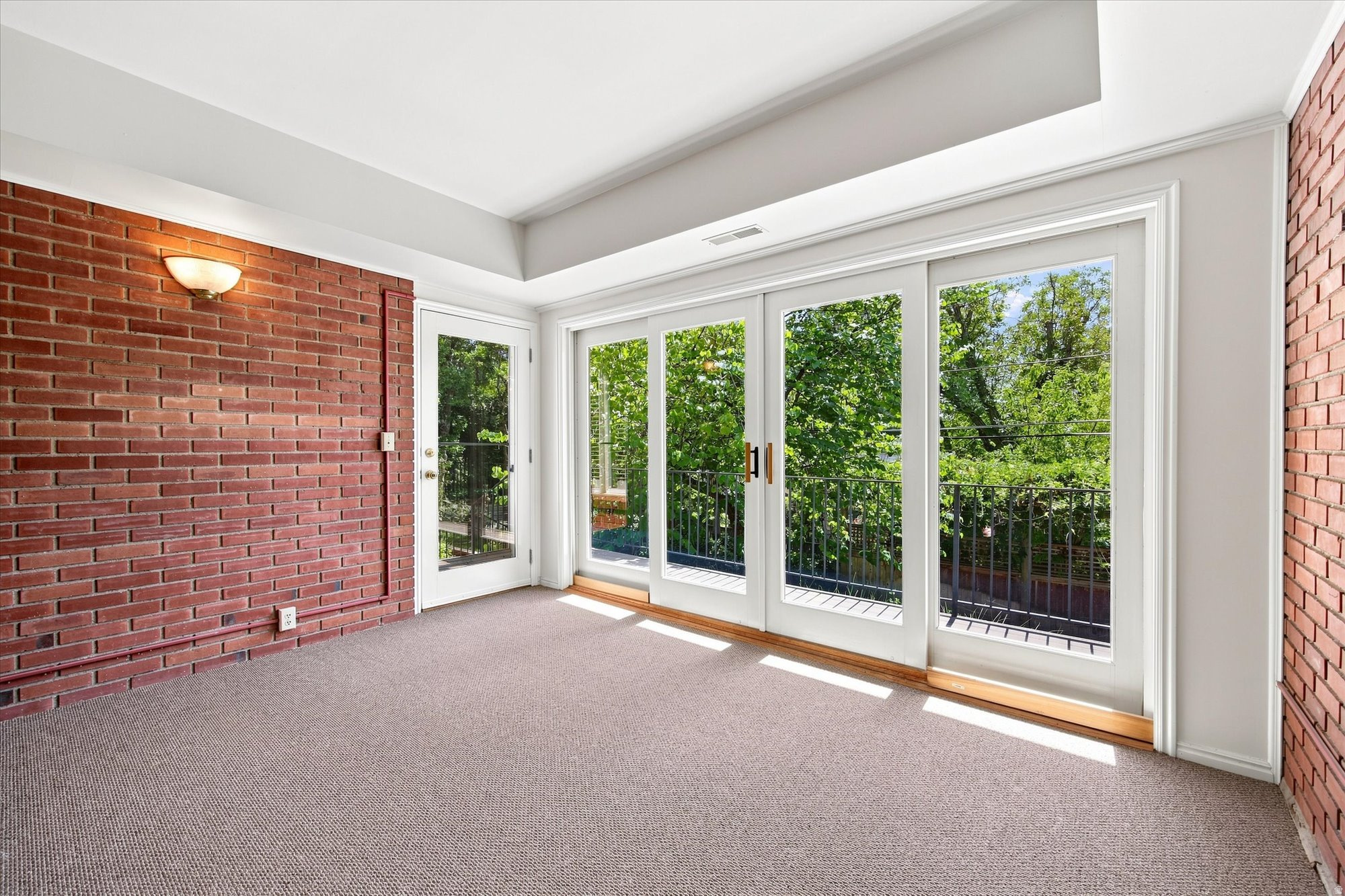 Empty sunroom with brick walls and large glass doors overlooking leafy trees.