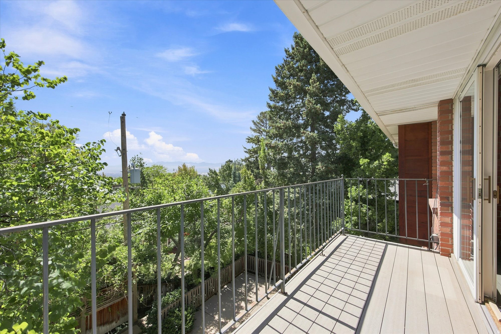 Balcony with metal railings overlooking leafy trees, distant mountains, and the city.