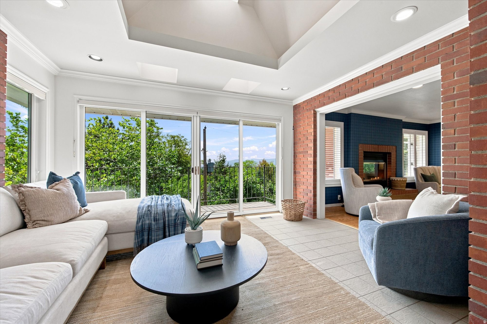 Living room with a vaulted ceiling, balcony doors, and a brick-framed fireplace room.