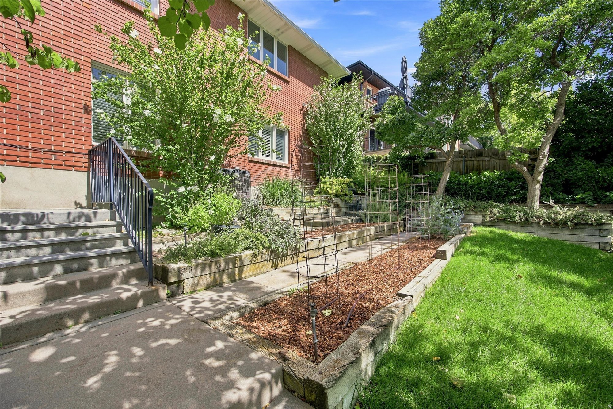 Brick home beside raised garden beds, a green lawn, and mature trees.