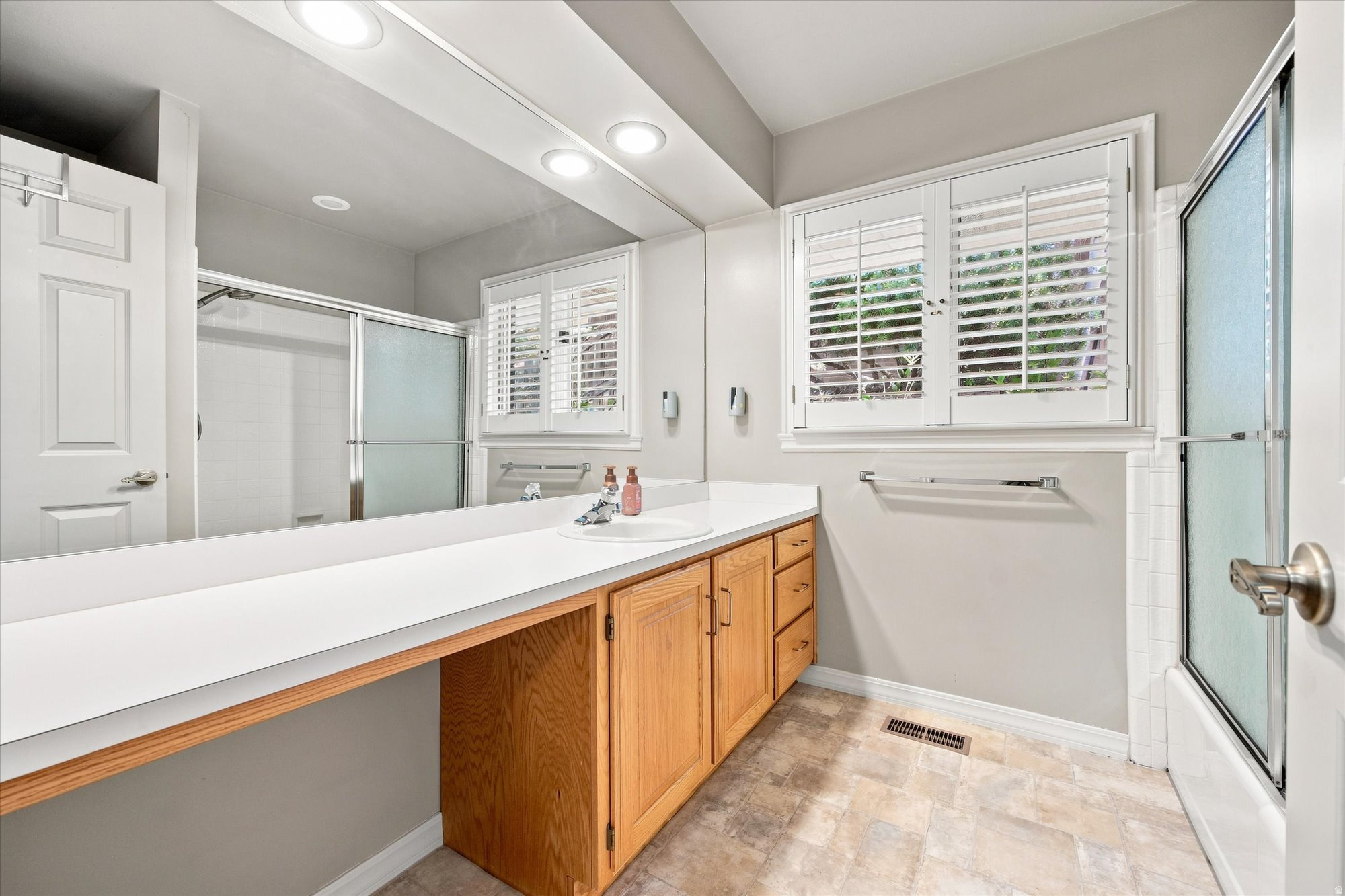Bathroom with a long white vanity, wood cabinets, mirrored wall, and glass shower enclosure.