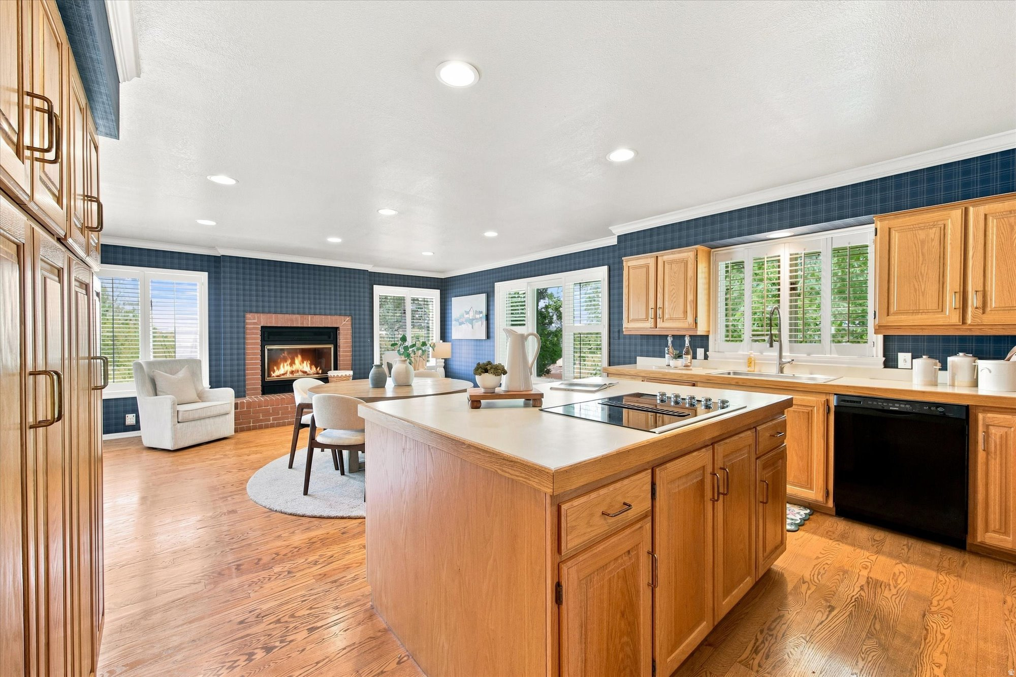 Kitchen with a large cooktop island, wood cabinetry, hardwood floors, and an adjoining sitting area with a fireplace.