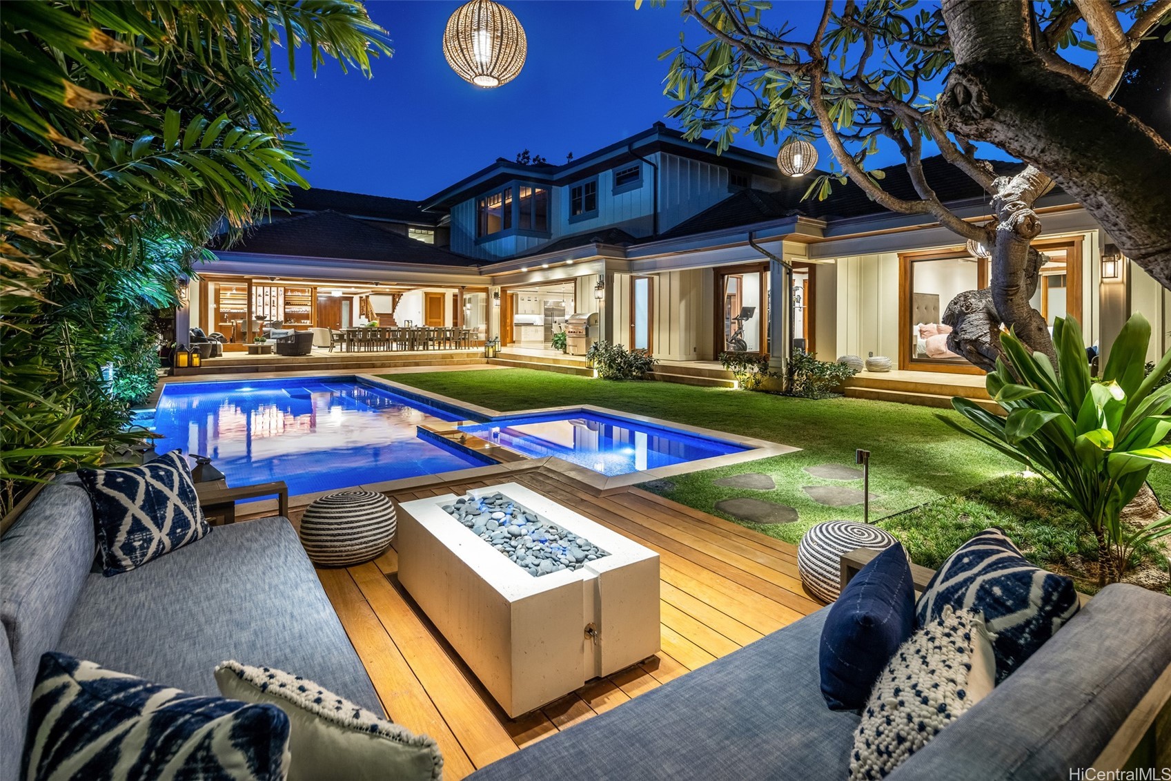 Modern home’s illuminated backyard pool, wood deck, and outdoor seating at dusk.