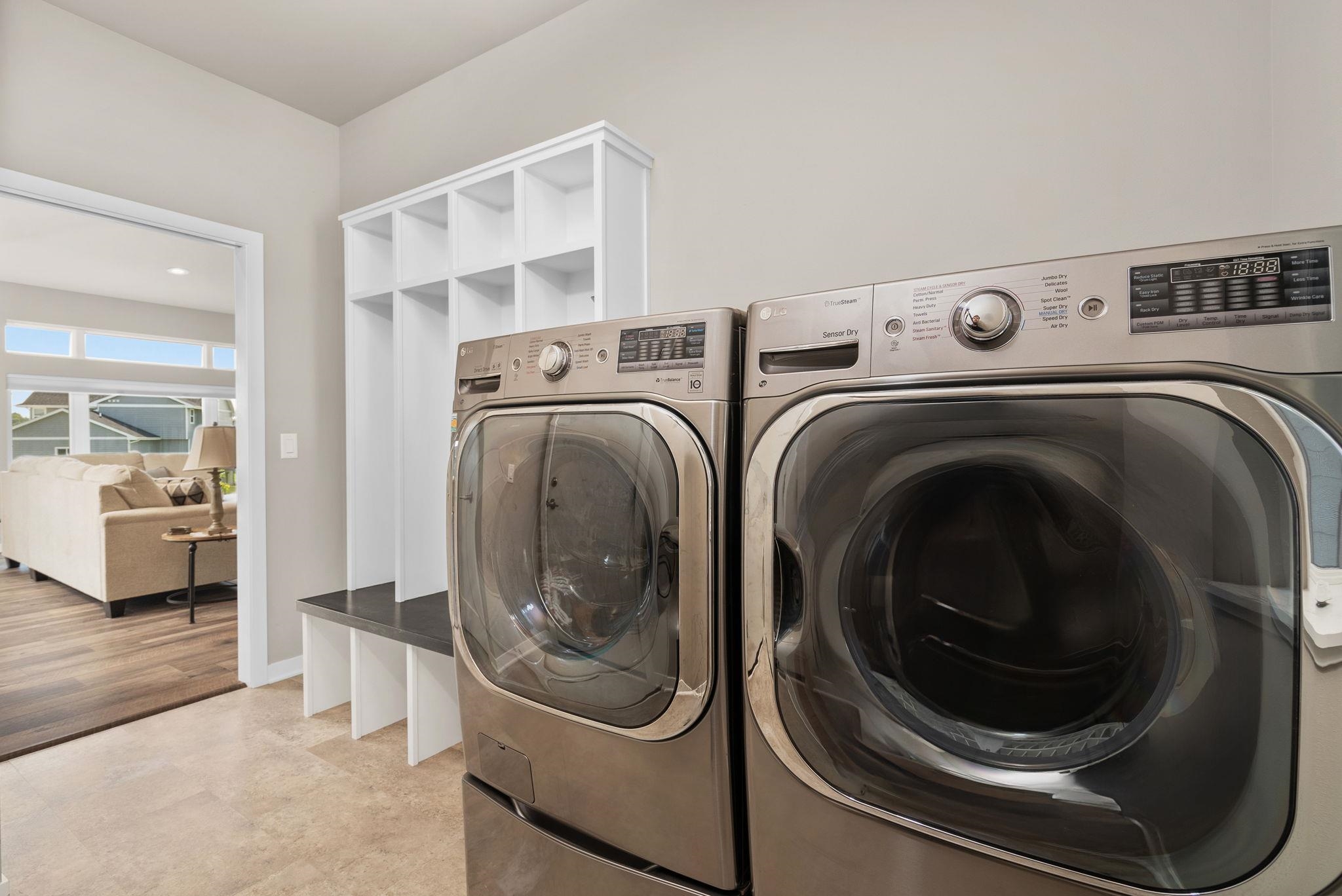 Laundry room with metallic front-loading washer and dryer beside white cubby shelving.