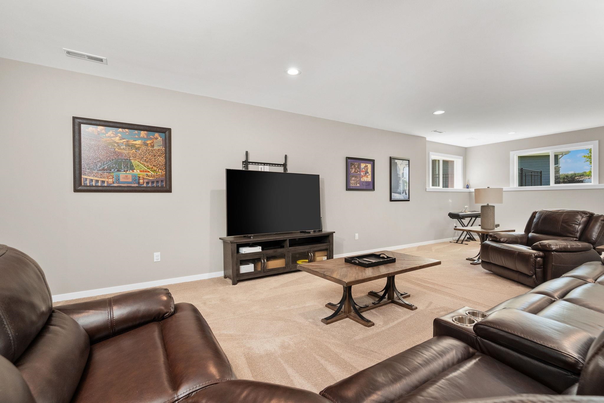 Furnished living room with leather sofas, a large television, and framed sports artwork.
