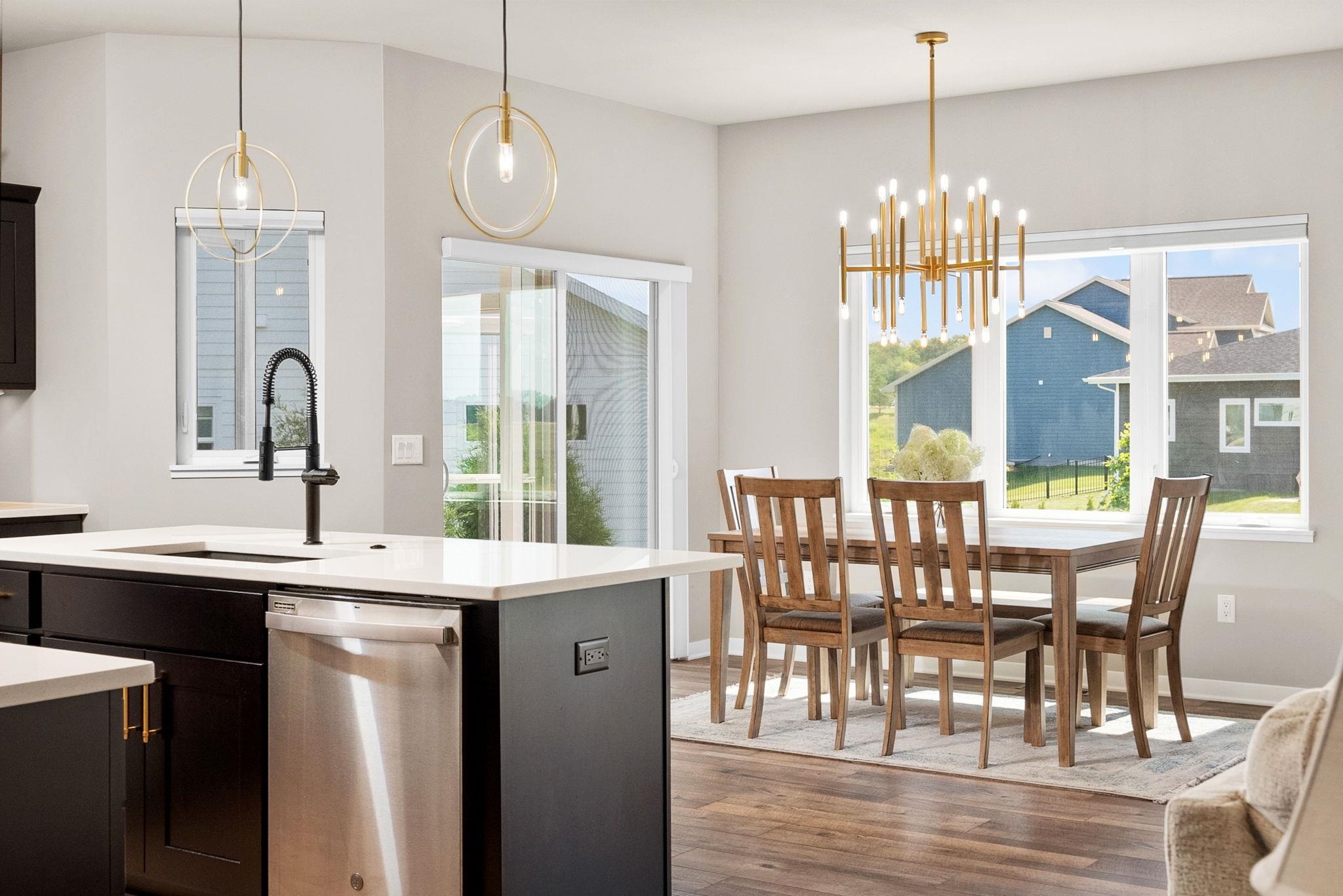 Open kitchen and dining area with a white island, dark cabinets, and wooden table beneath a gold chandelier.