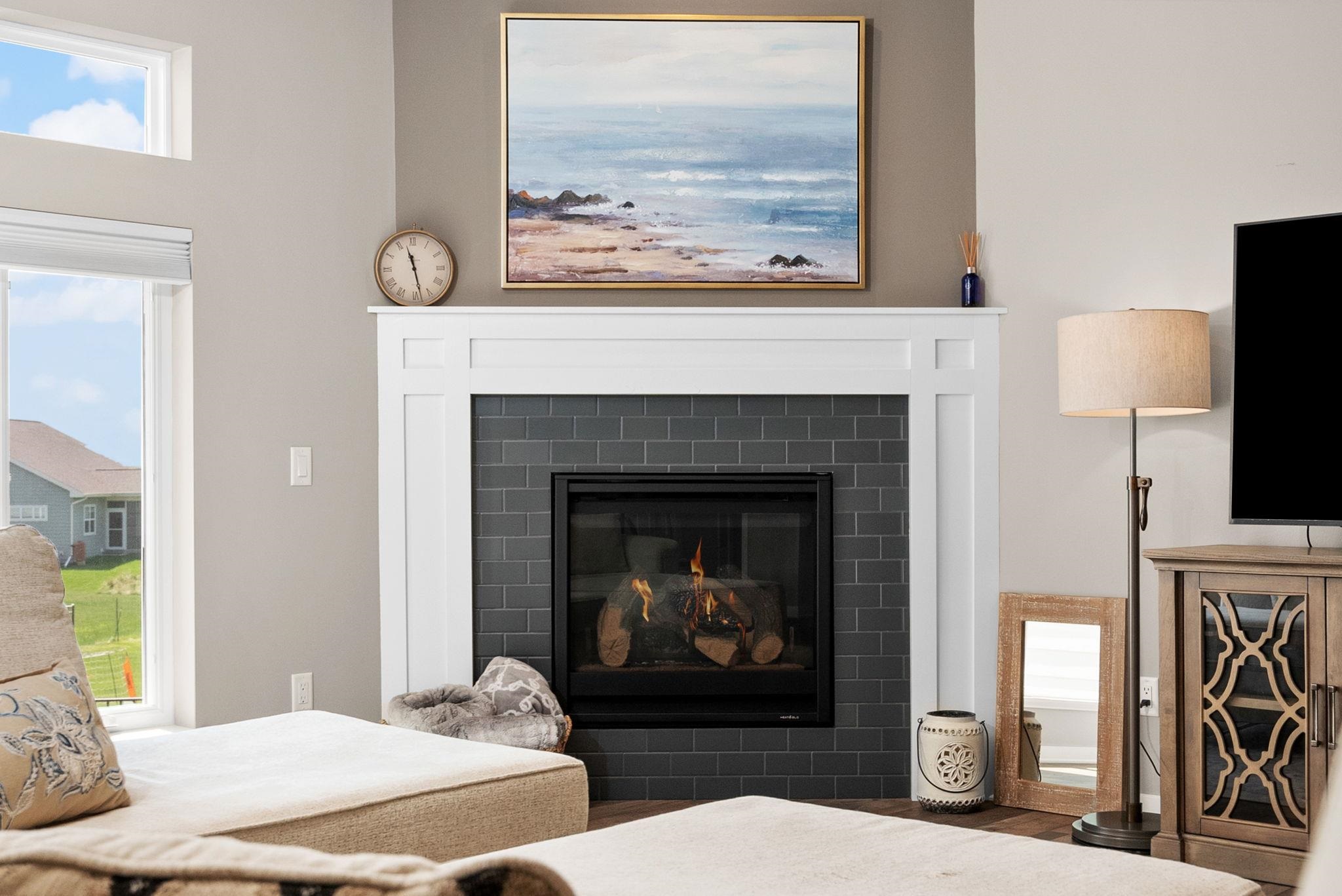 Furnished living room with a lit fireplace, dark tile surround, and ocean painting above the mantel.