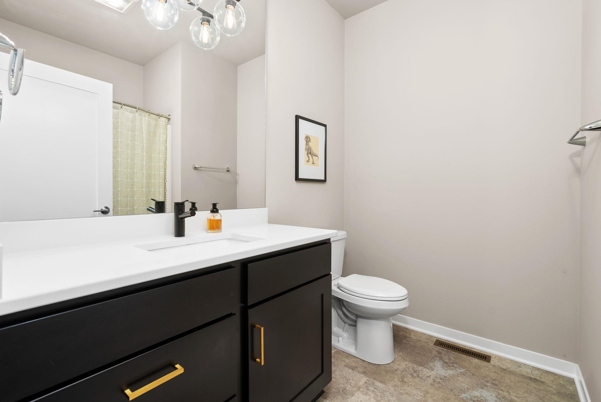 Bathroom with a dark vanity, white countertop, black faucet, and toilet beside a curtained shower.