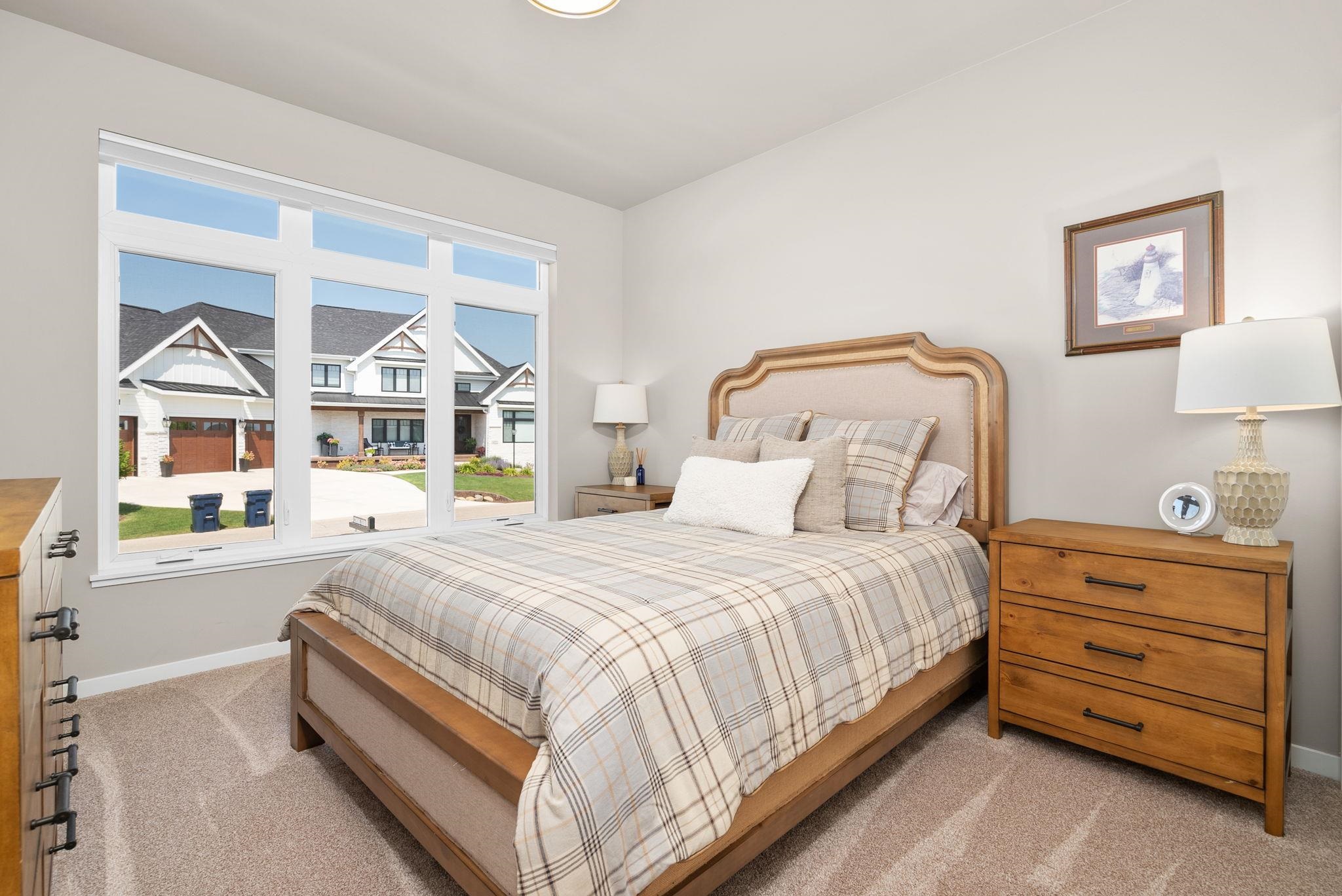 Bedroom with plaid bedding and wide windows overlooking neighboring homes.