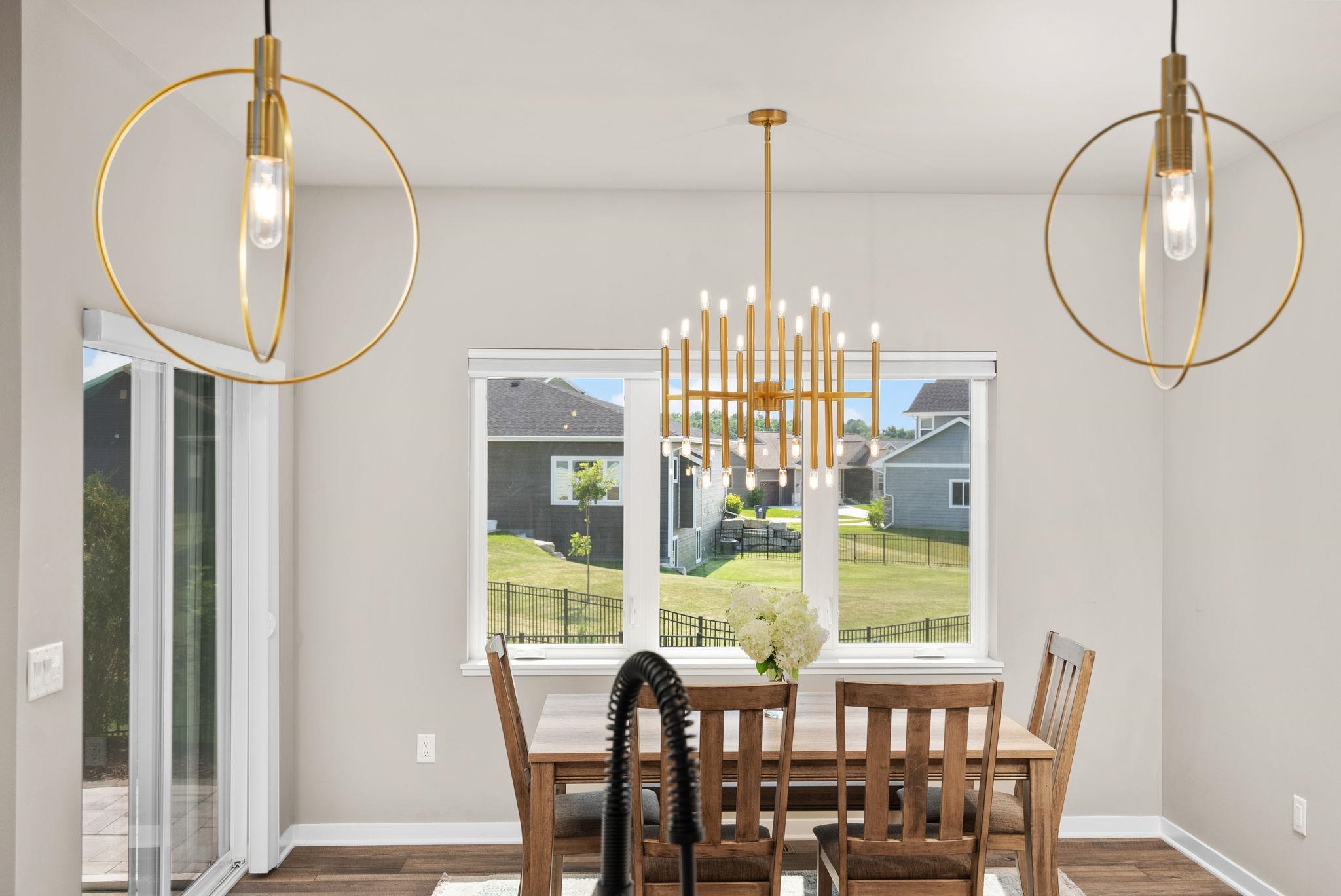 Dining area with a wooden table, gold pendant lights, and a large window overlooking a fenced backyard.