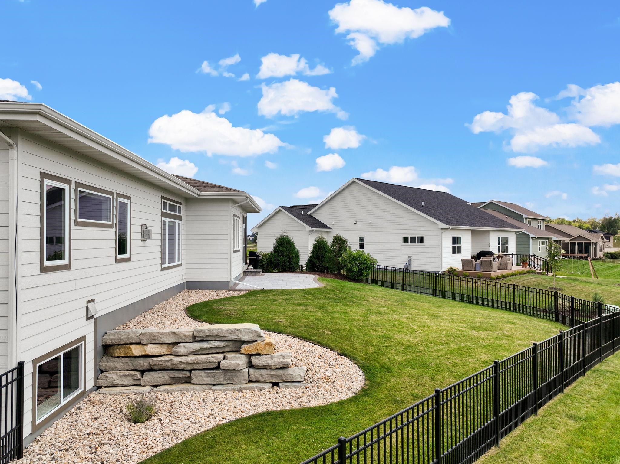 House and fenced backyard with a green lawn, stone landscaping, and a paved patio.