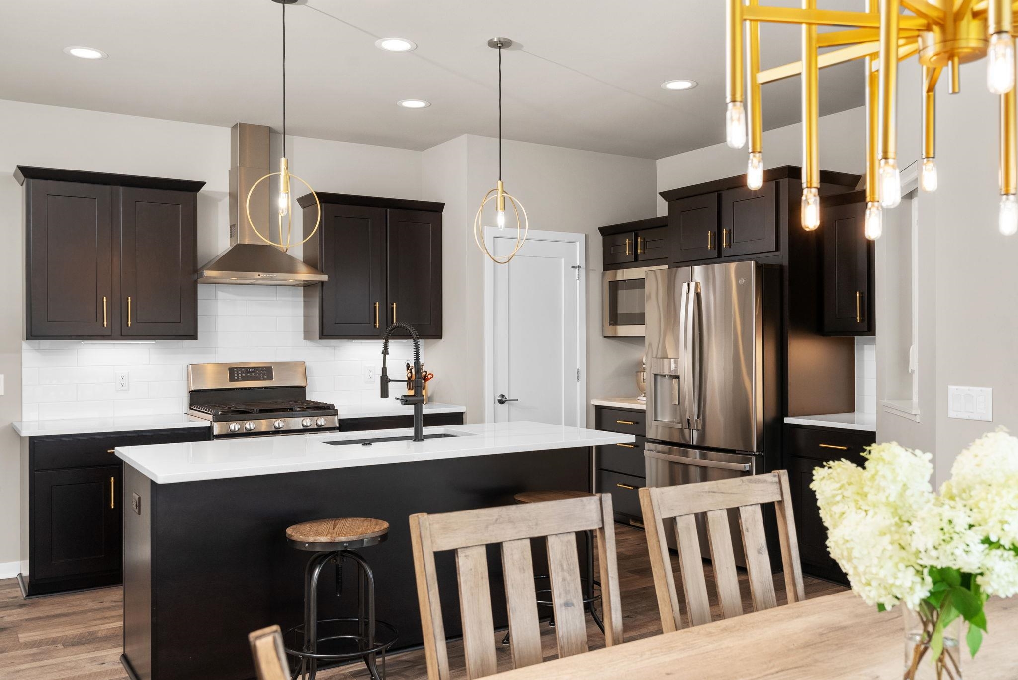 Modern kitchen with dark cabinets, stainless steel appliances, and a white island with gold pendant lights.