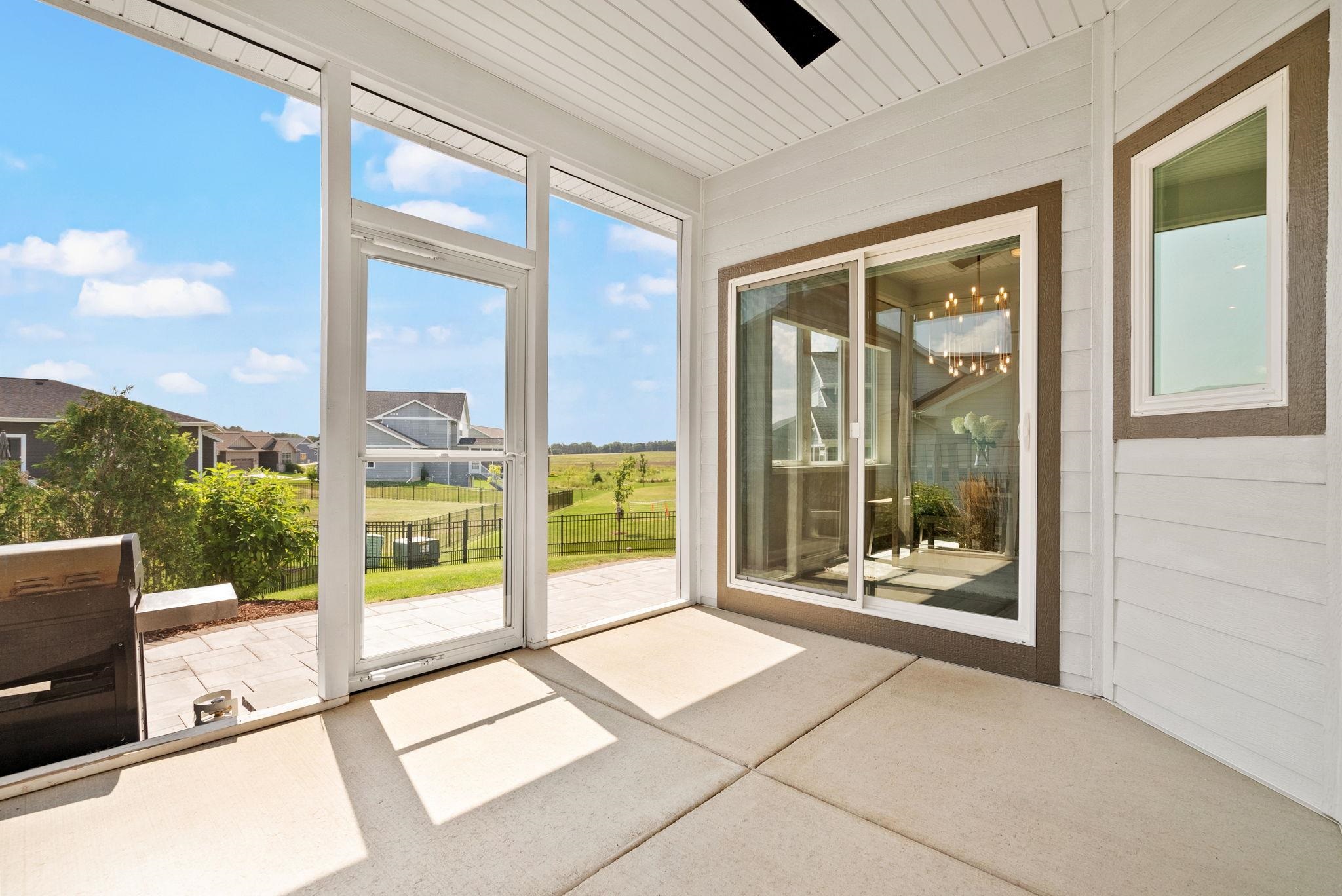 Covered patio with sliding glass doors and barbecue grill overlooking a fenced yard and grassy field.