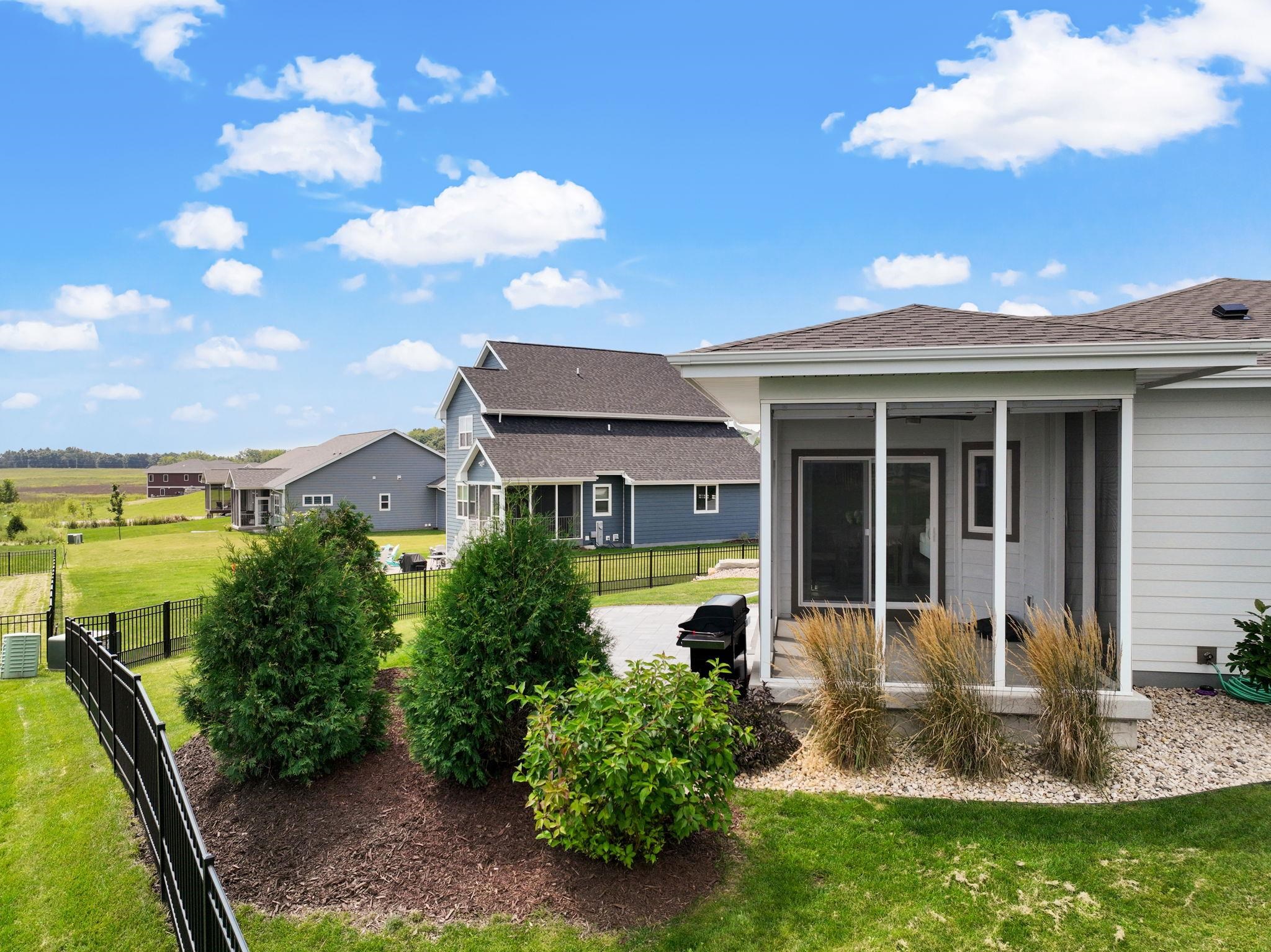 Home’s screened rear porch and landscaped yard with black fencing and neighboring houses beyond.