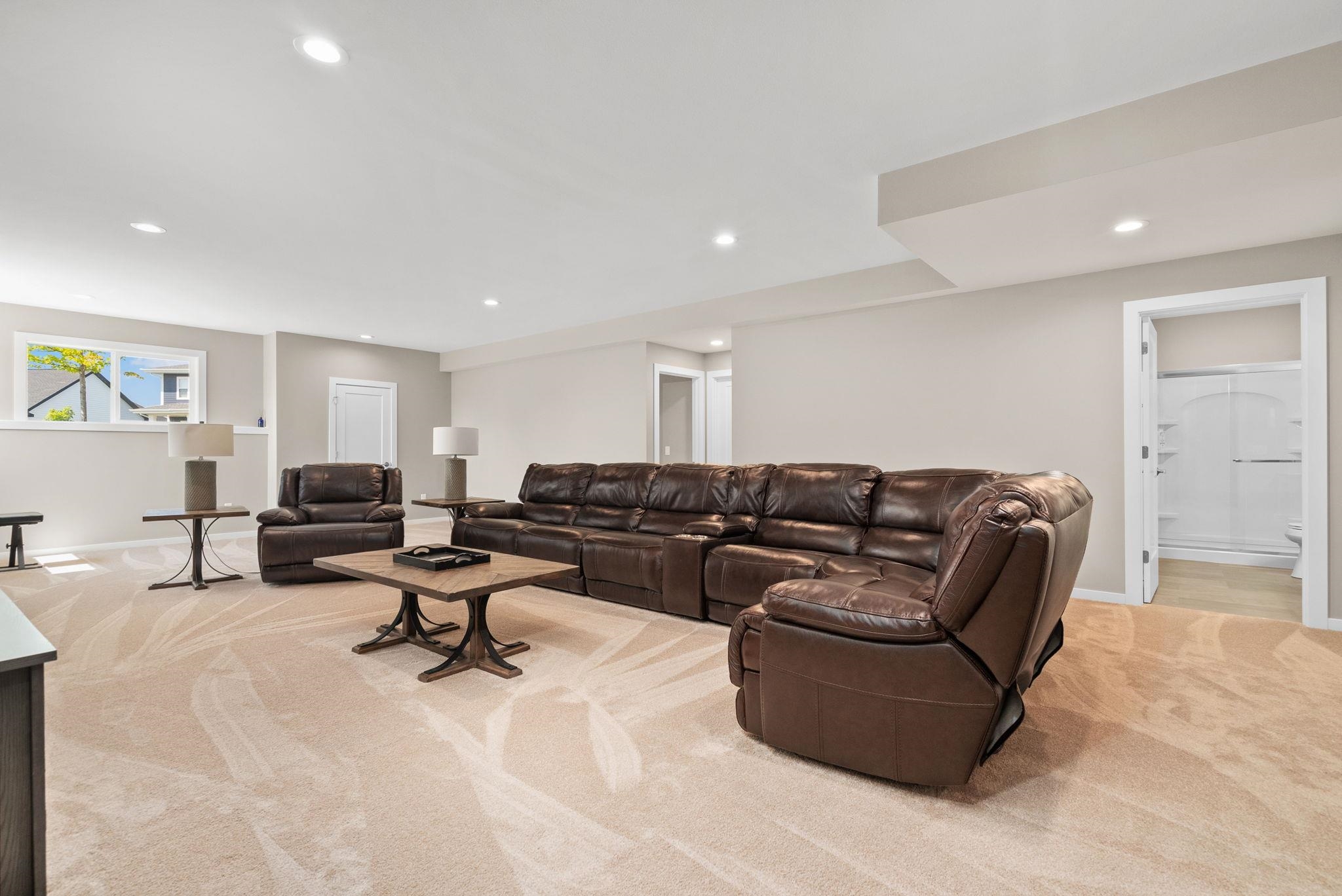 Furnished living room with a large brown leather sectional, matching recliner, and patterned beige carpet.