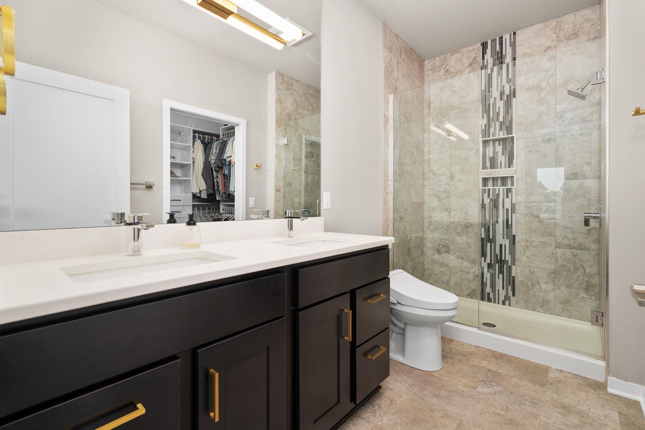 Bathroom with a dark double vanity and glass shower featuring a vertical mosaic tile accent.