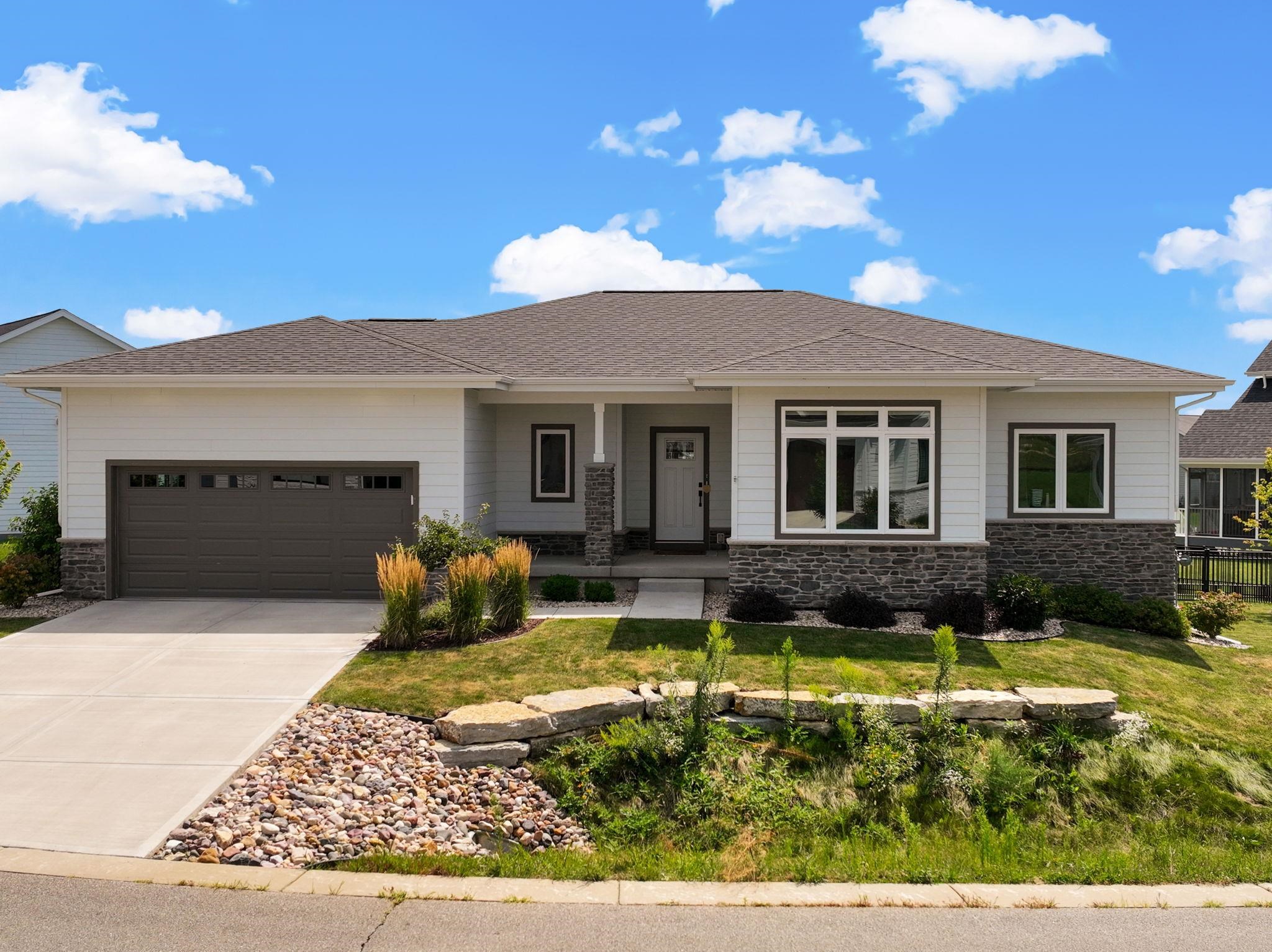 Single-story house with a dark two-car garage, stone accents, and landscaped front yard.