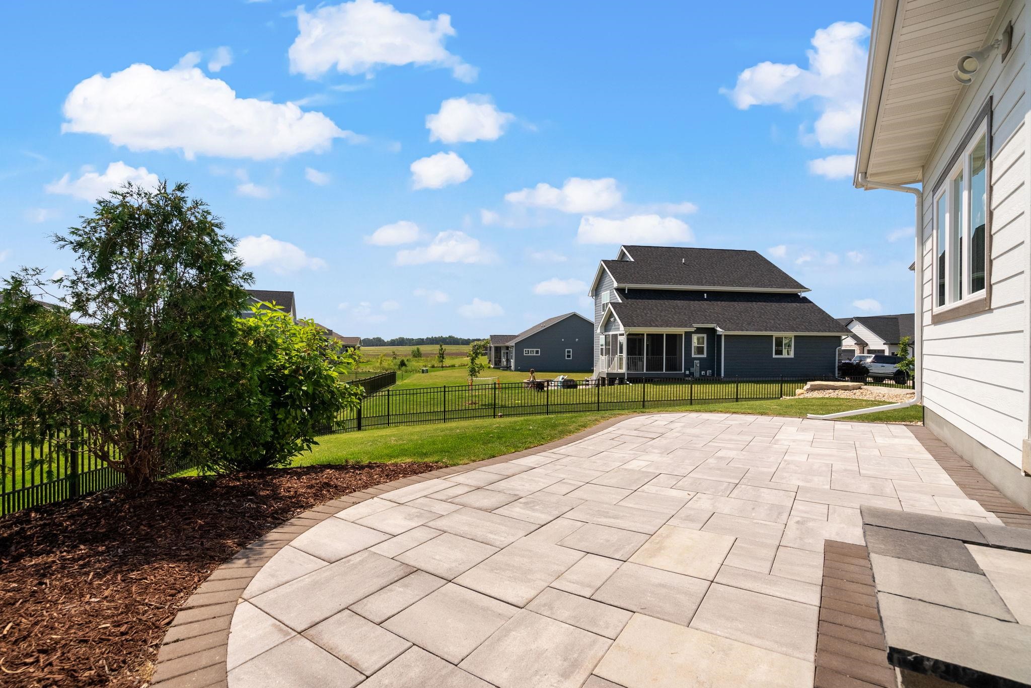 Backyard patio with a wide paver terrace, fenced lawn, and open fields beyond.